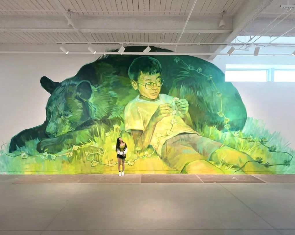 Emily Ding brings together animals, figures, flora, and the natural world to explore themes of vulnerability, growth, belonging, and human connection. Her latest mural at the Trout Museum of Art is part of TAG, an exhibition celebrating street, graff