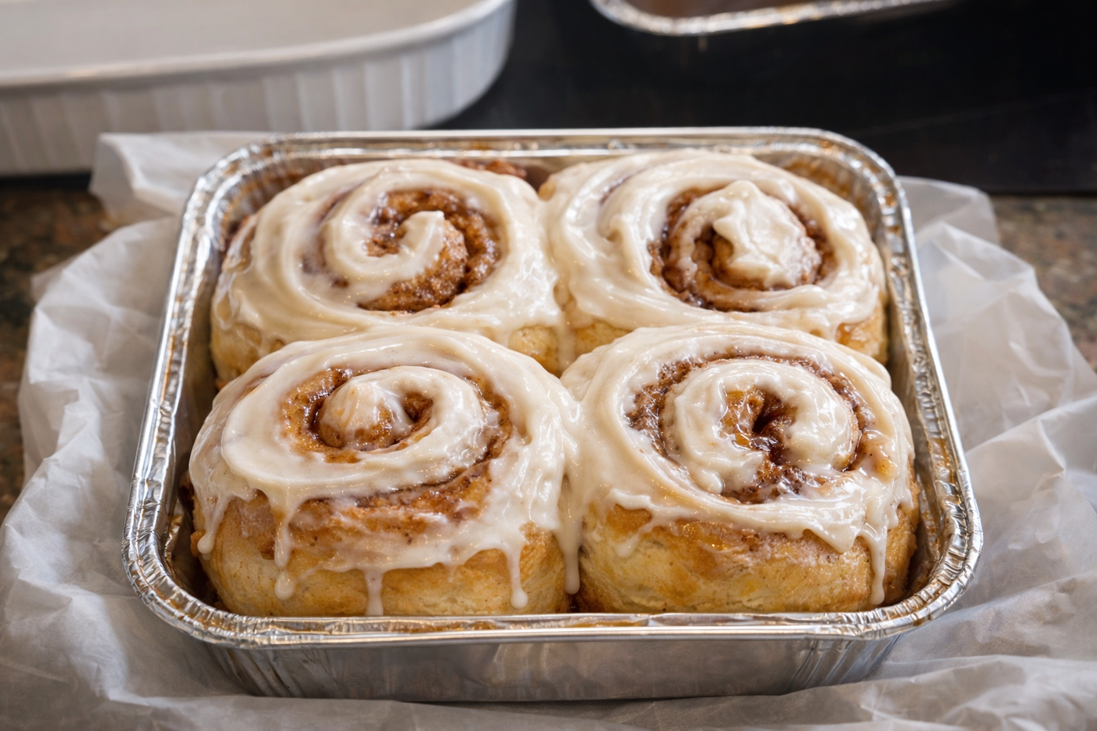 A baking tray with four cinnamon rolls covered in white icing.