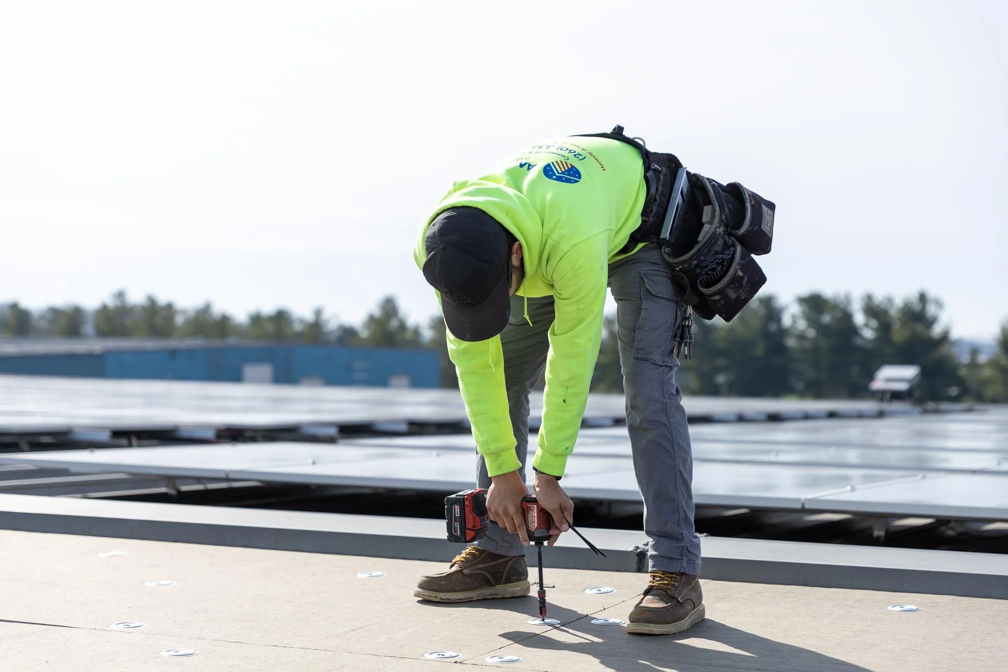 A worker in a black cap and yellow hoodie making repairs on a commercial roof near Elkhart, IN
