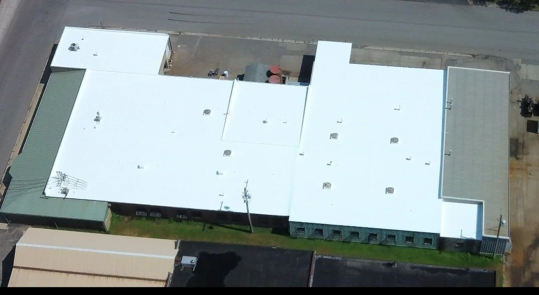 Aerial view of a large commercial building with white flat roof and rooftop units