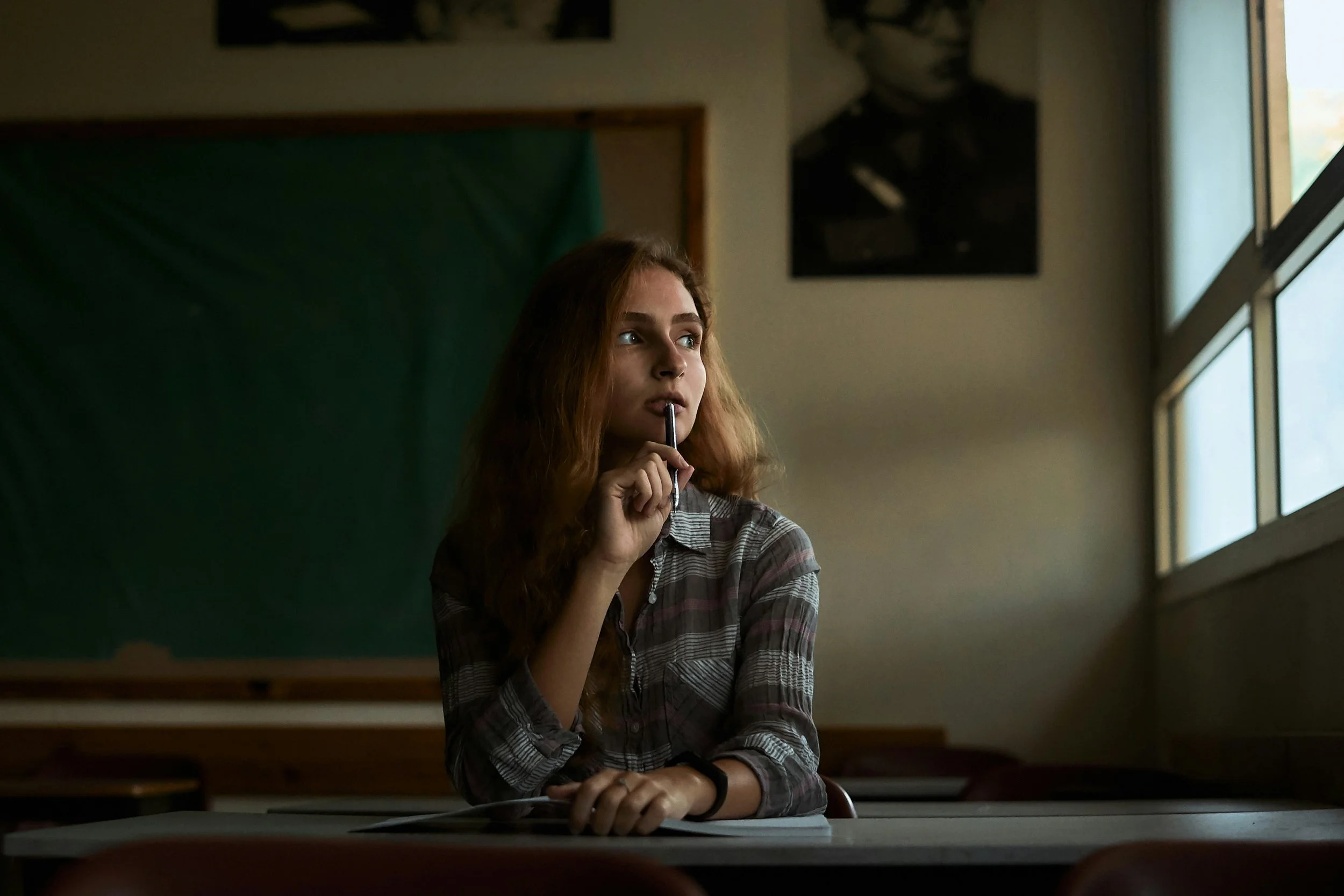 College student sitting at a desk in a classroom, looking out the window, thinking about EMDR therapy