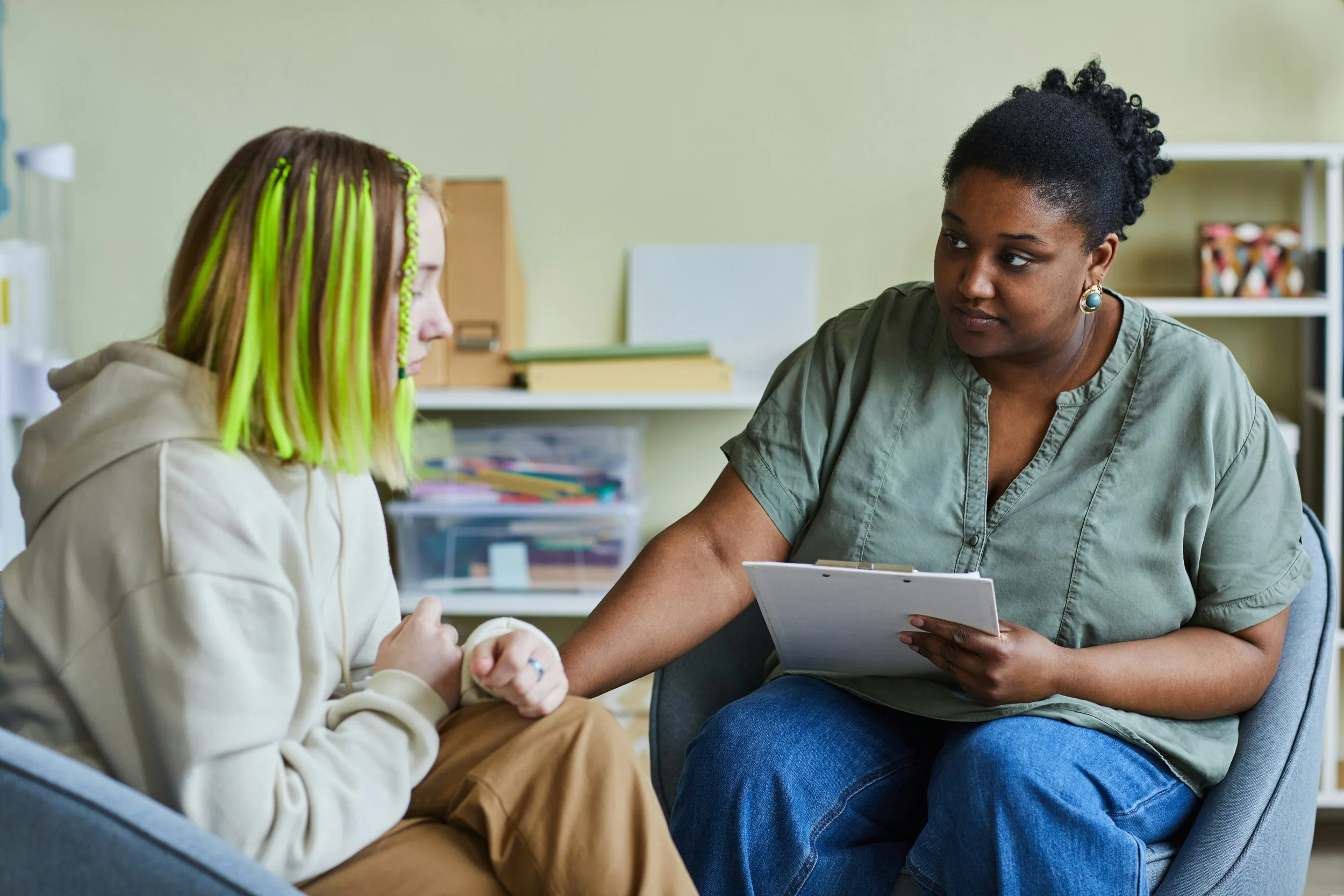 Teen therapist turned toward a teenage client and listening during a counseling session