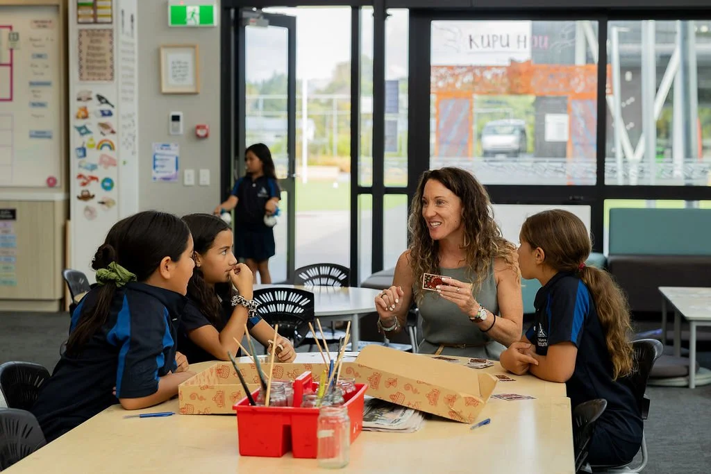 A teacher playing Māori board game Kaupapa with four young girls in a classroom.