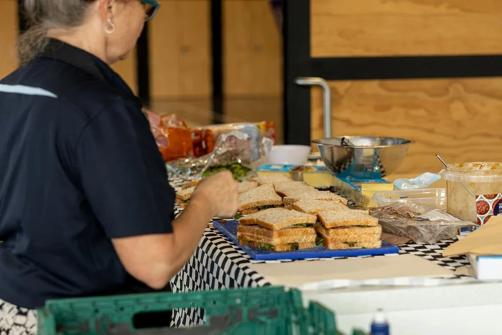 A person in a black shirt preparing school sandwiches on a table with various ingredients and food containers around.