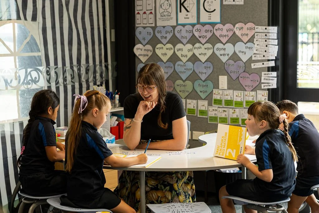 Teacher and four students working together at a round table in a classroom.