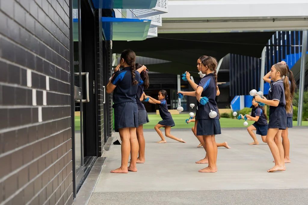 Group of school children dressed in navy blue uniforms, practicing poi outdoors.