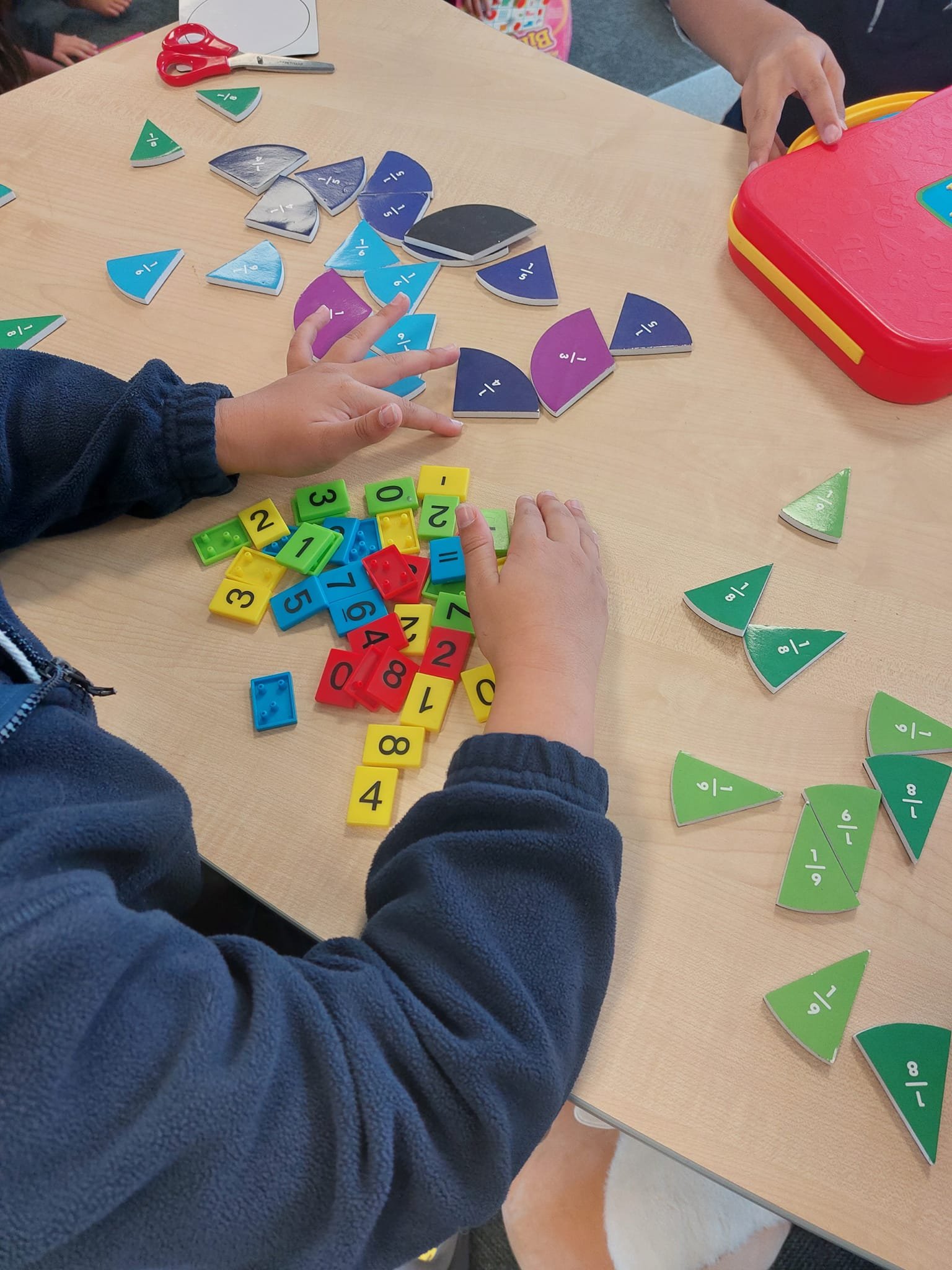 Children playing with fraction and number tiles on a wooden table.
