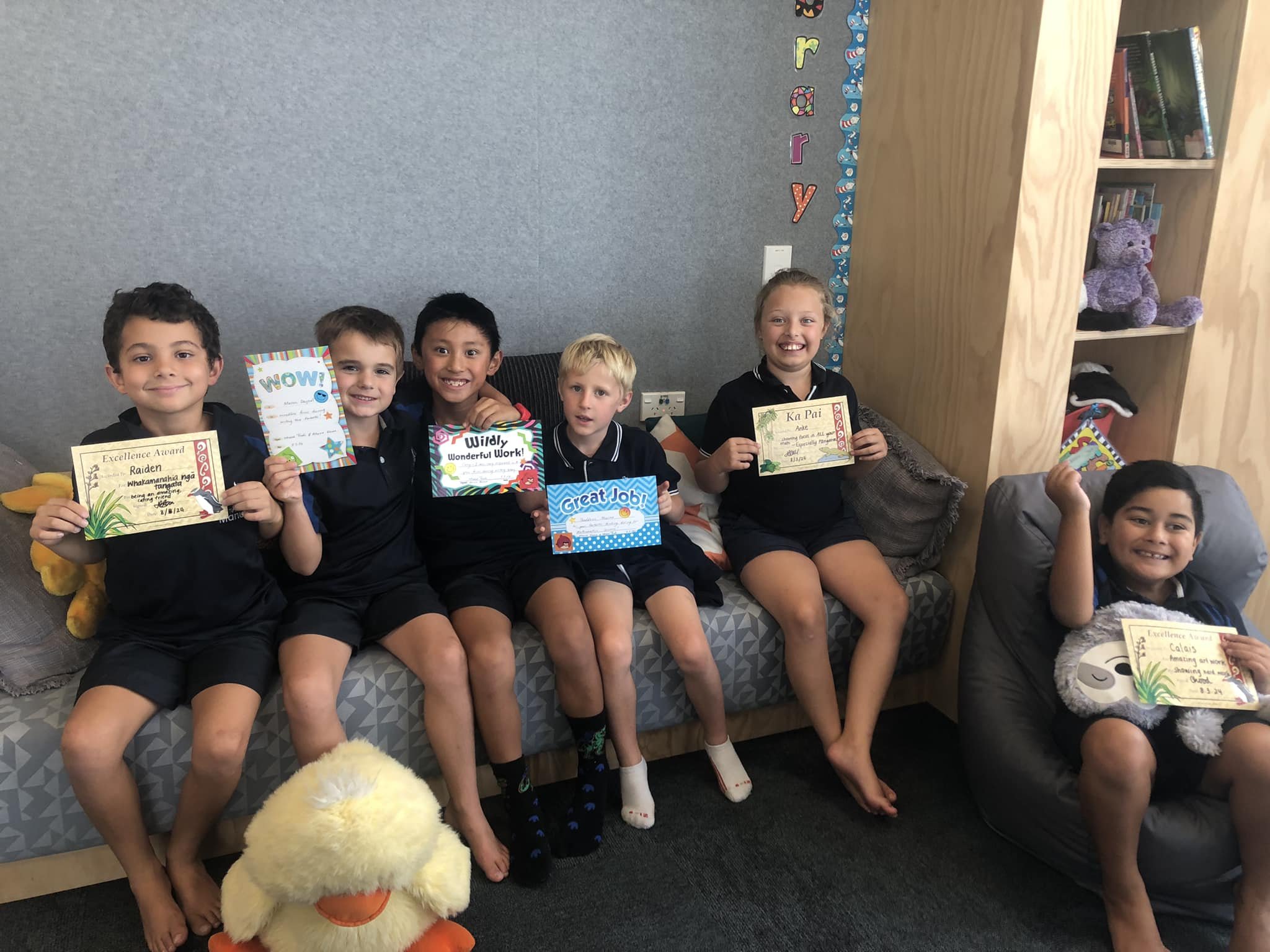 Group of children sitting on a bench, each holding a certificate, smiling