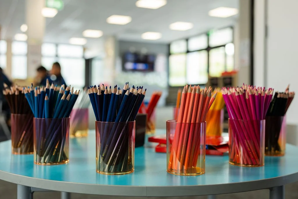 Colorful colored pencils in transparent cups on a blue table in a bright room.