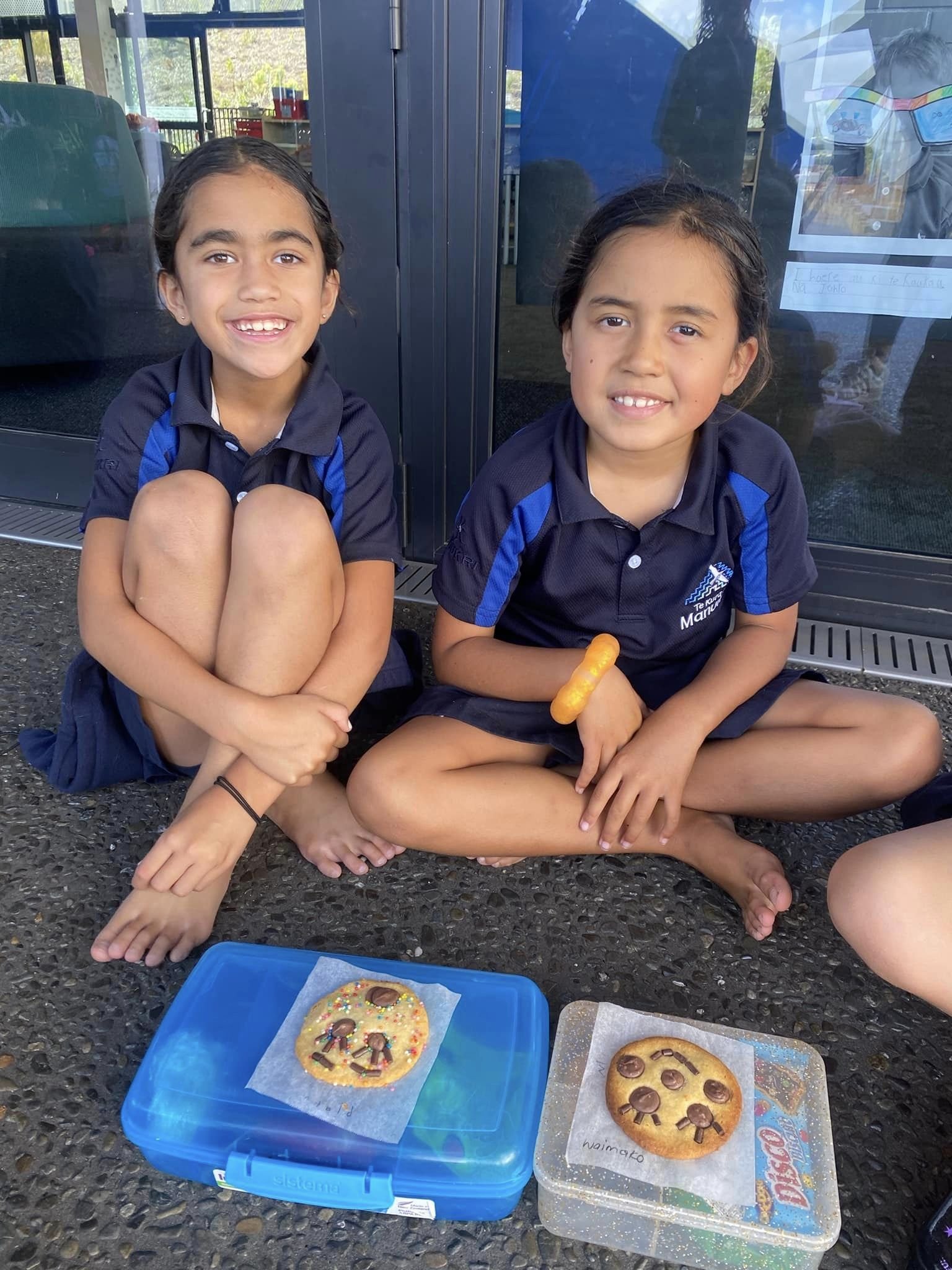 Two children sitting on the floor with decorated cookies in containers in front of them.