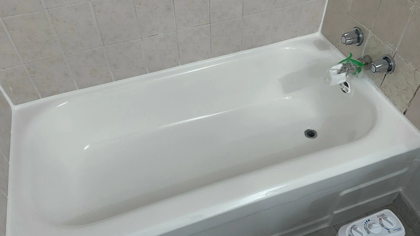 Empty white bathtub in a tiled bathroom with a drain and fixtures.