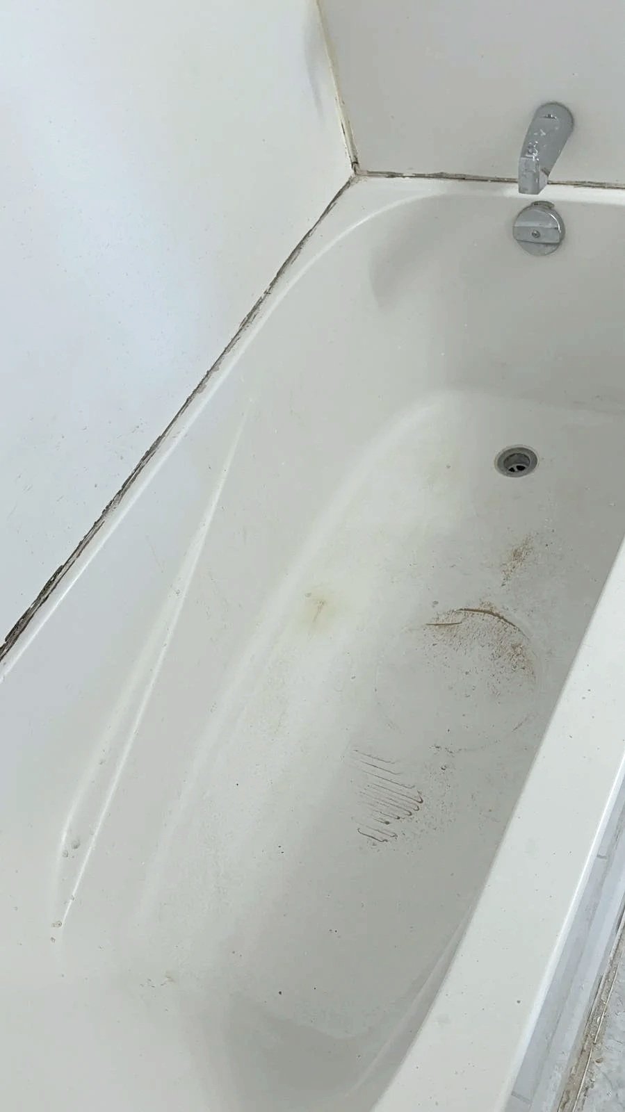 Empty white bathtub with some dirt and scratches, situated next to a wall with visible grout lines.