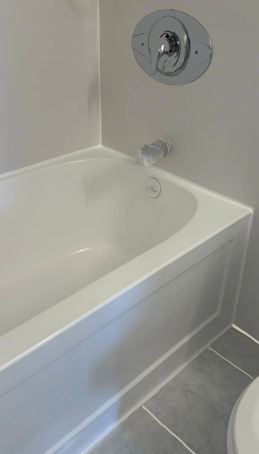 Bathroom with a white bathtub, a round chrome shower faucet, and a plastic-wrapped water spout that appears to be a makeshift shower head or pipe extension.