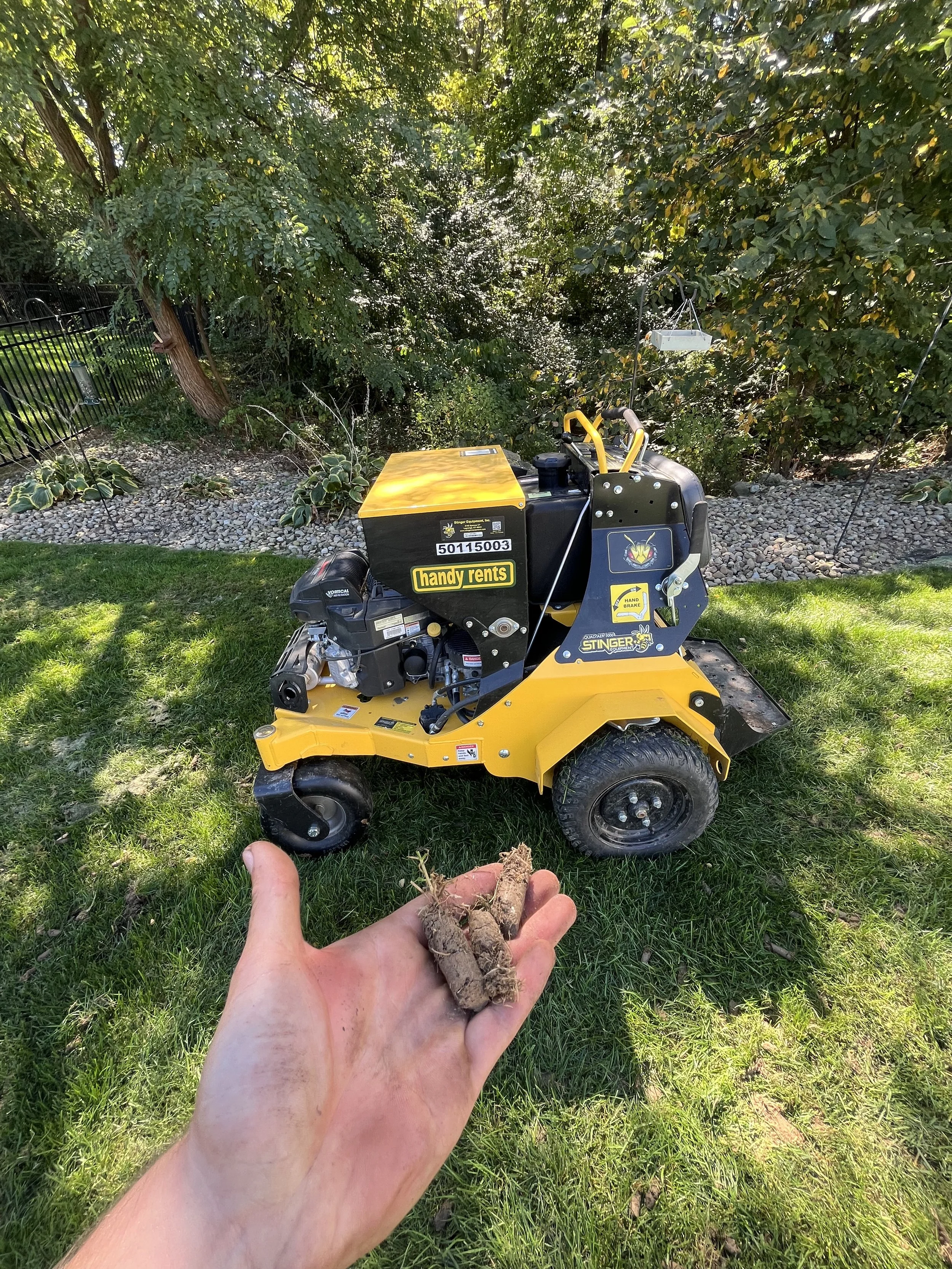 An employee holding aeration plugs with an aeration machine behind.