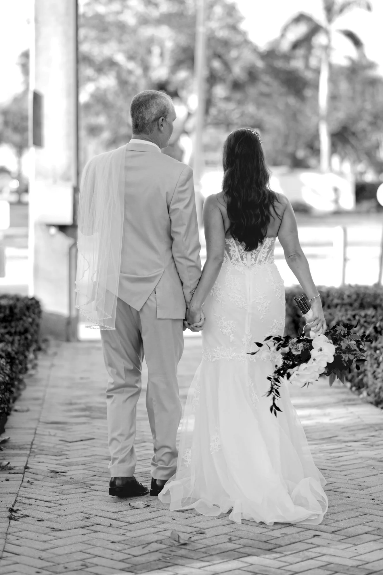 Black and white photo of a couple walking away hand in hand on a brick path in Stuart