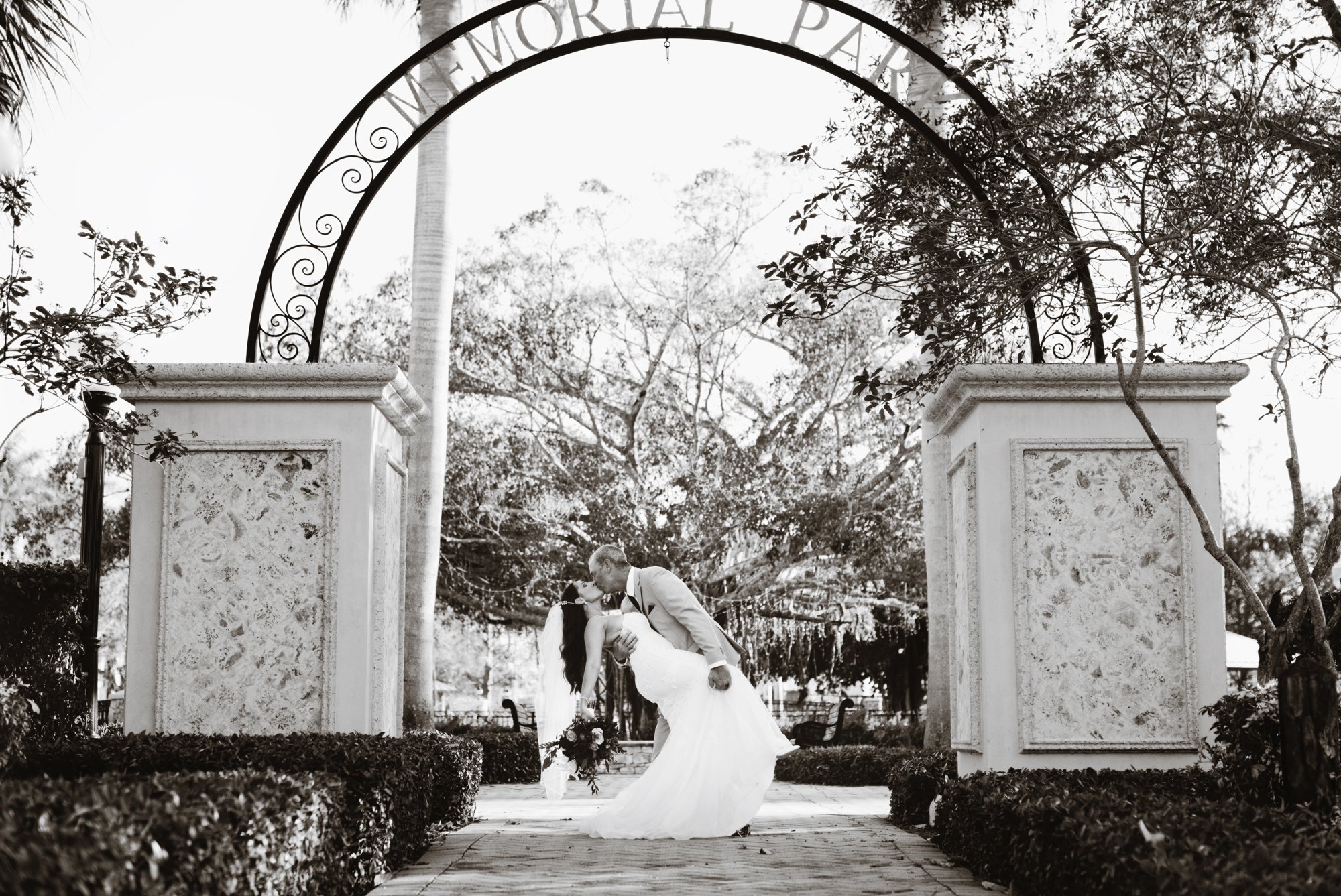 Black and white dip kiss beneath the Memorial Park arch in Stuart