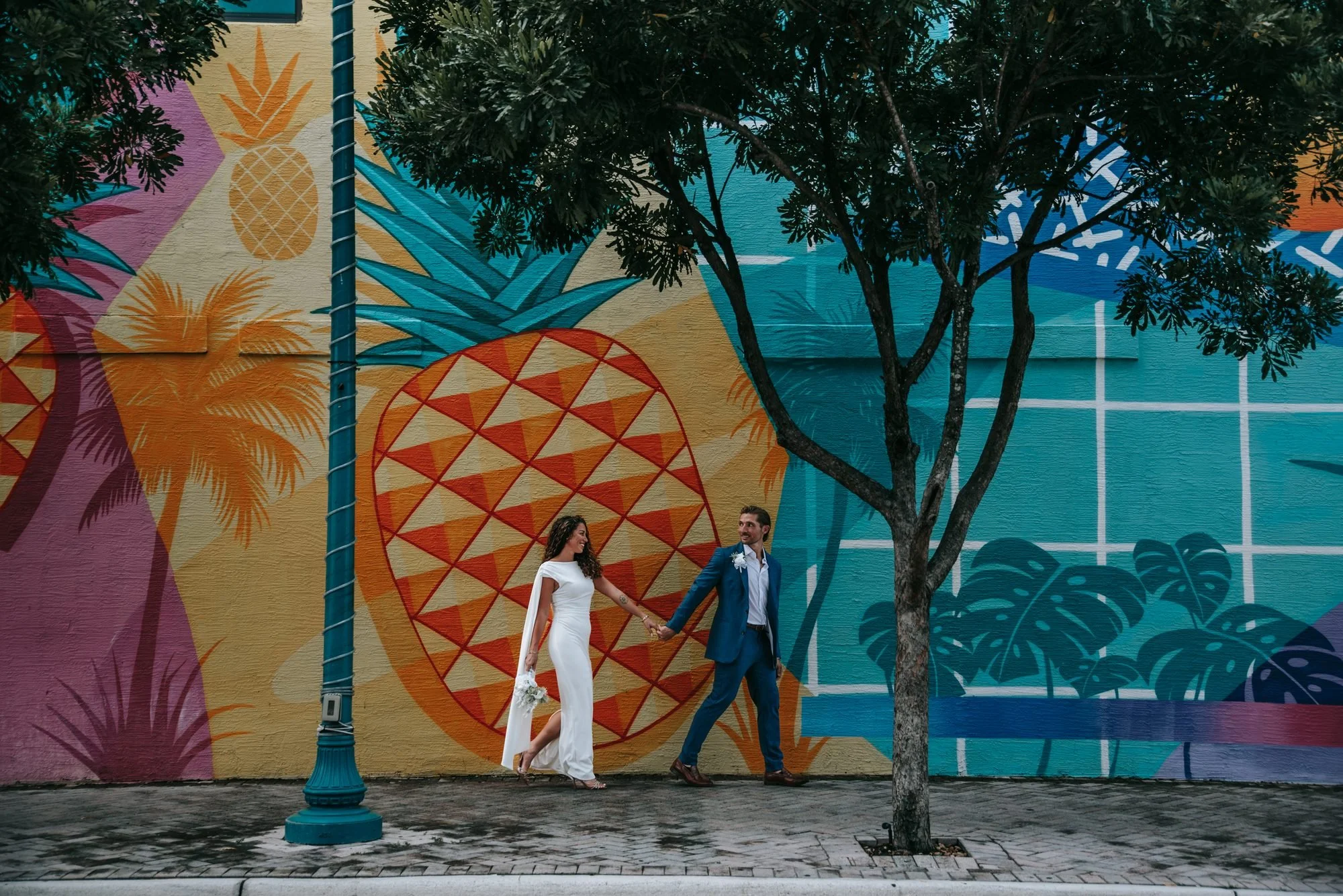 Newlyweds walking past a colorful pineapple mural in the Pineapple Grove Arts District in Delray Beach