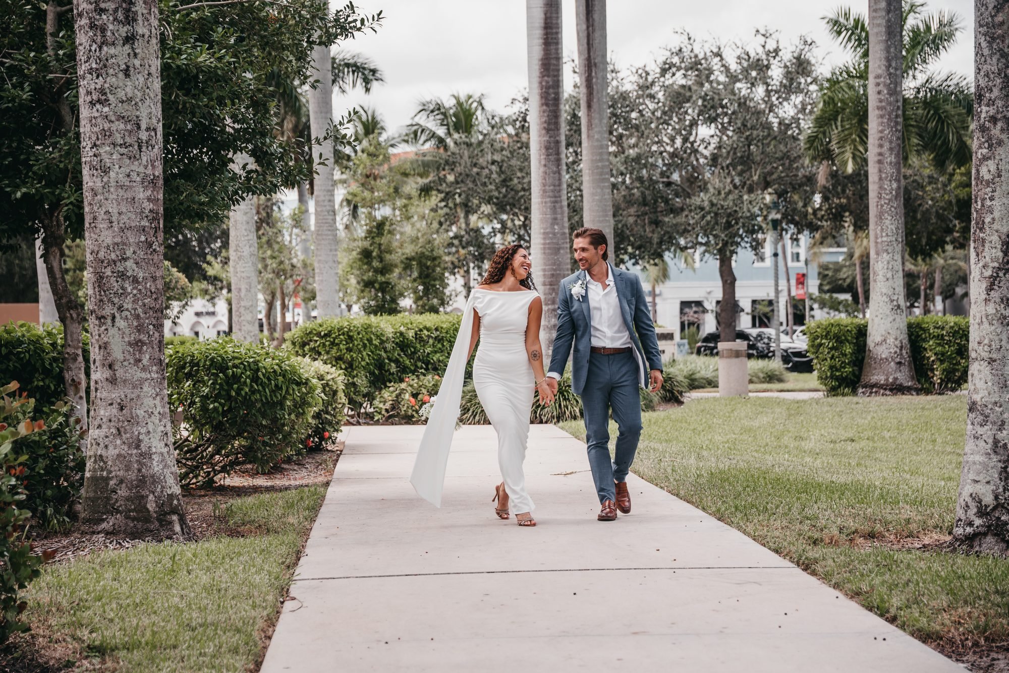 Bride and groom walking hand in hand along a palm-lined path at Old School Square in Delray Beach