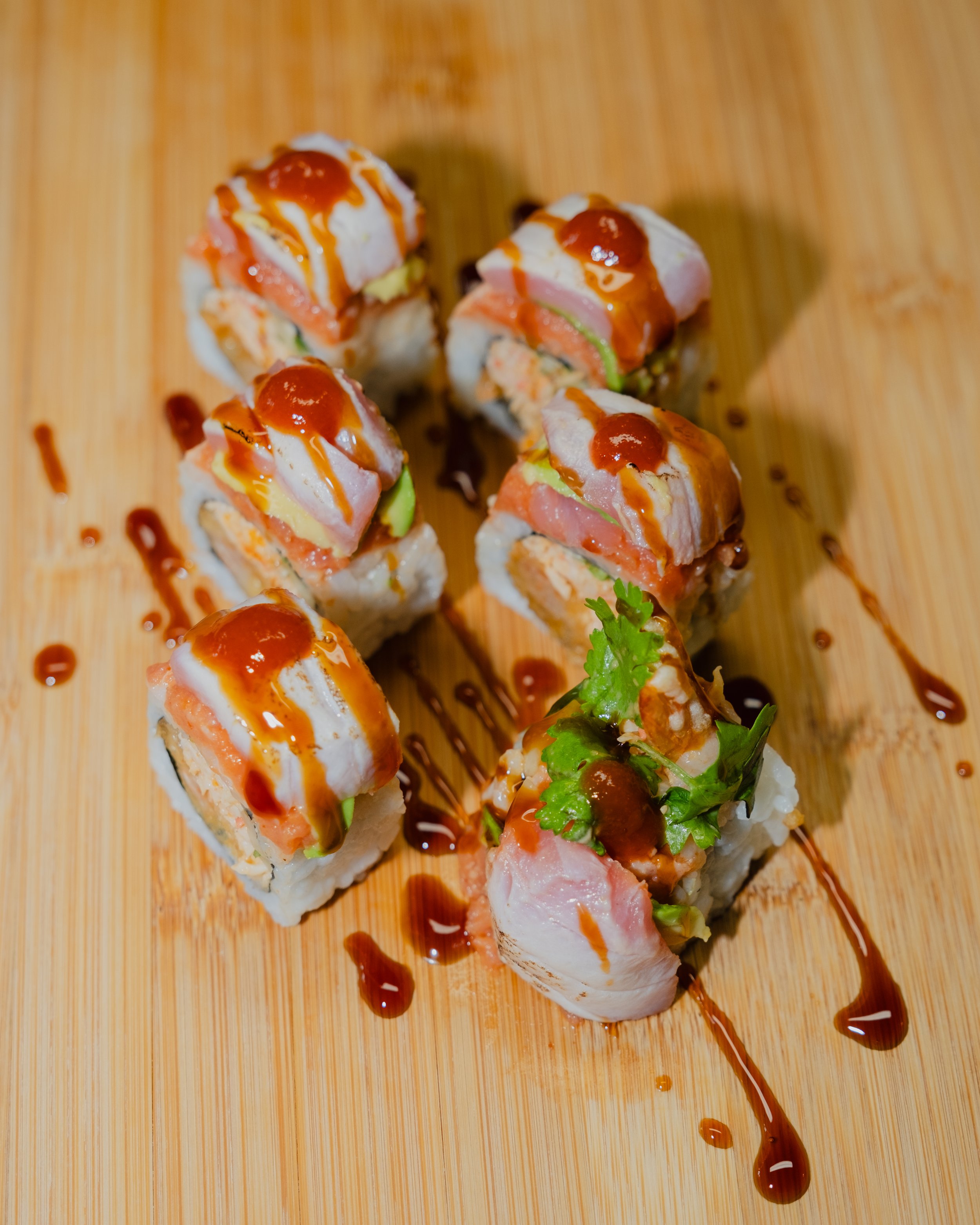 Sushi rolls with fish, vegetables, and sauce on a wooden serving board