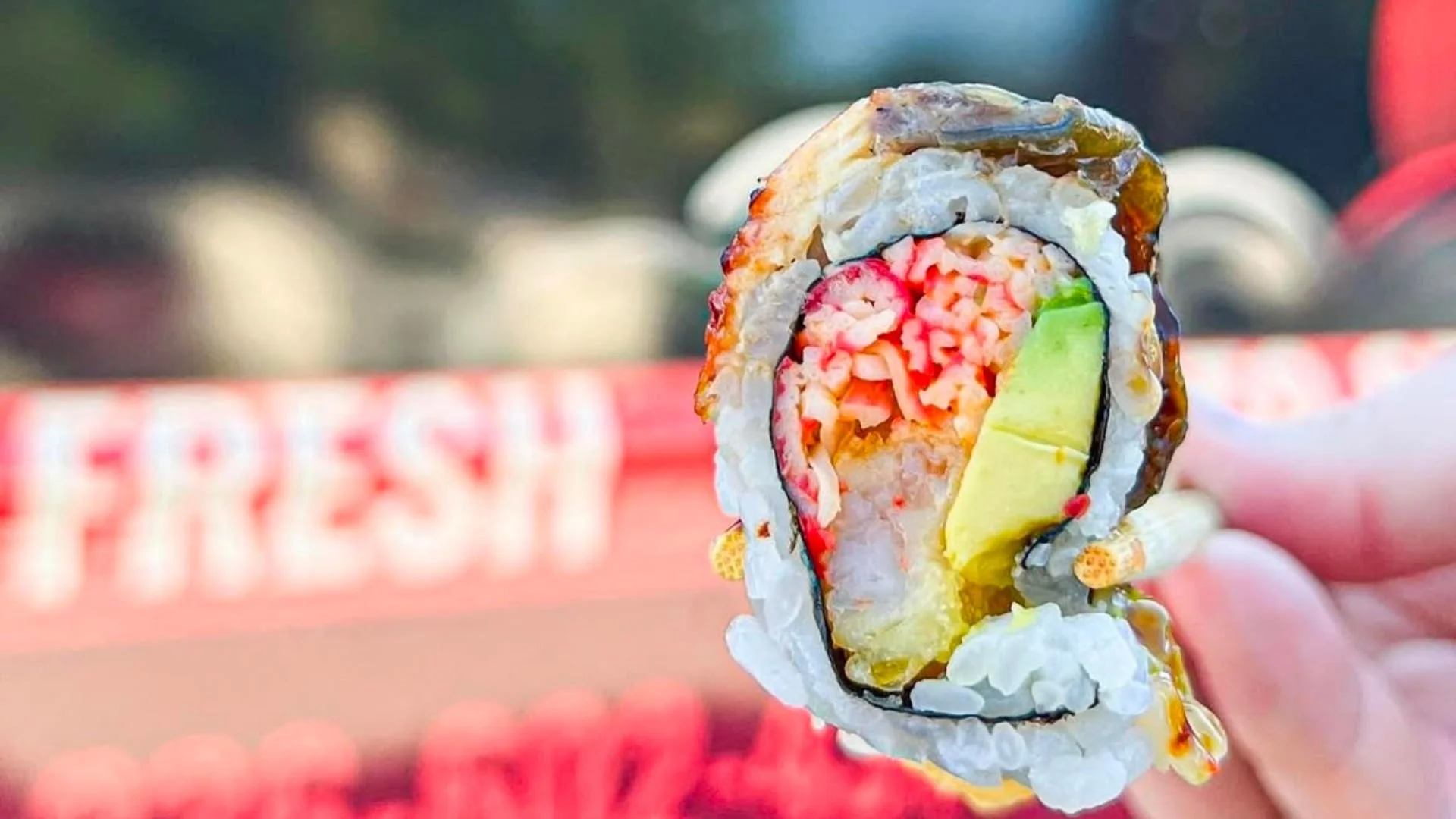 Close-up of a sushi roll with visible ingredients including rice, crab, avocado, and cucumber, with a blurred background.
