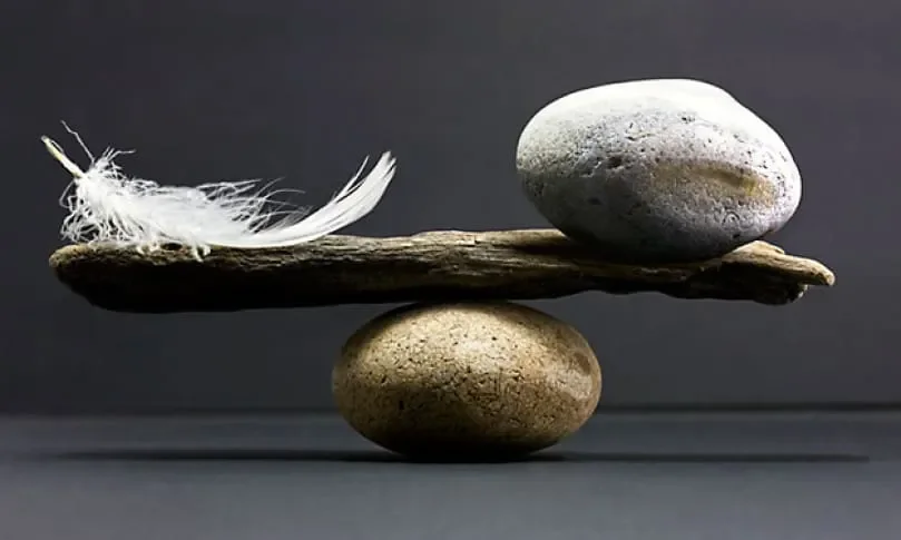 A balanced arrangement of two stones, a piece of driftwood, and a white feather on a dark background.