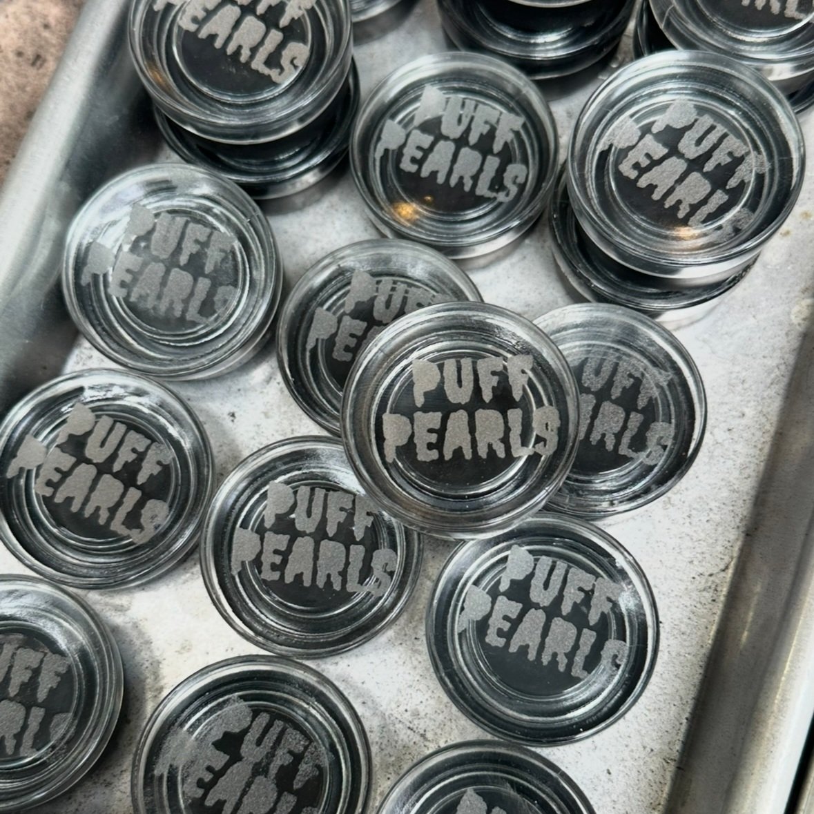Glass jars with black labels reading 'PUFF PEARLS' stacked on a metal tray.