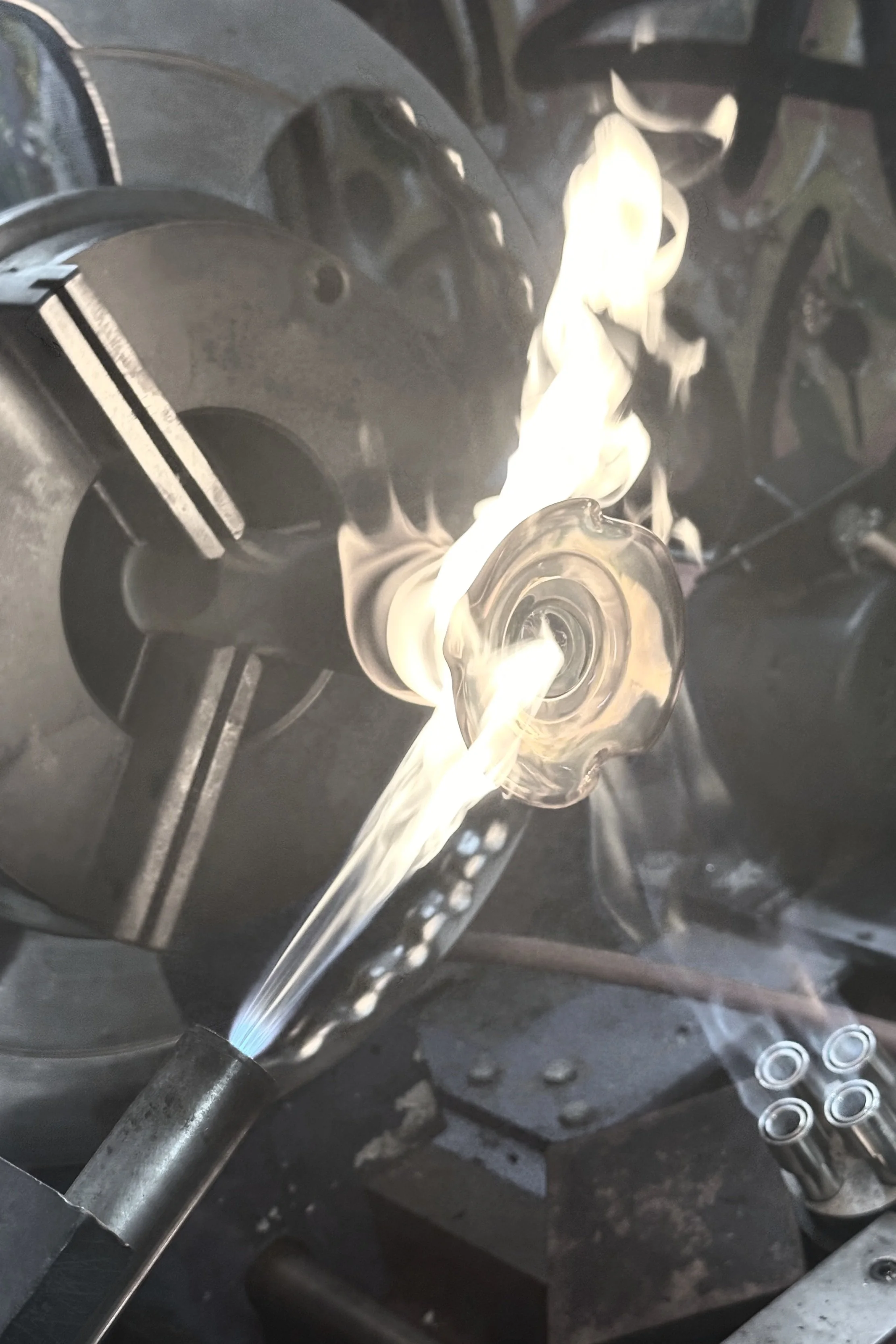 Glassblowing process with a glass piece shaping over a flame, working on hot glass at a workshop.