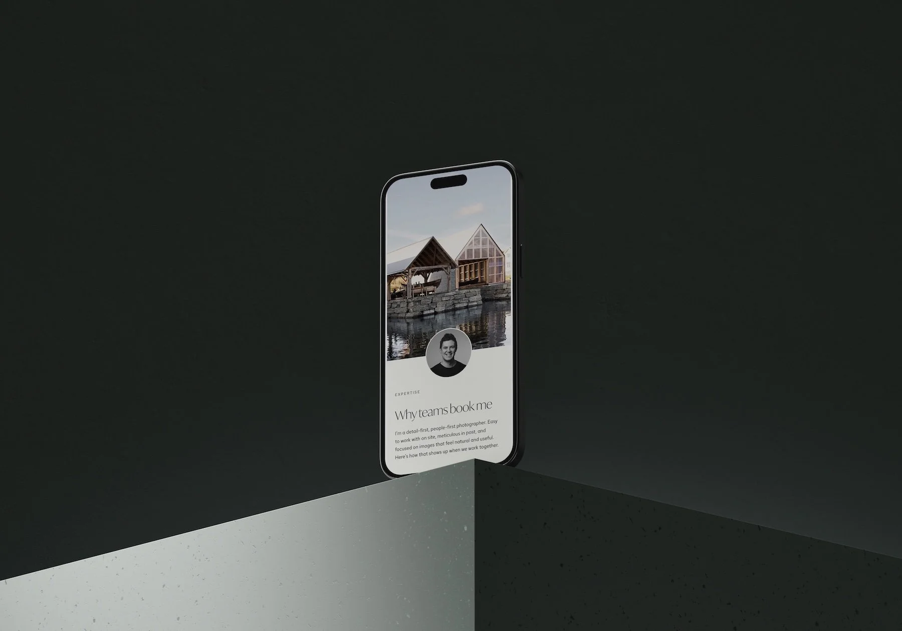 iPhone sitting on a concrete shelf showcasing the about section of Alex Coppo's photography website made in Launch Labs, minimal layout, profile shot overlaid on architectural photography image of Norwegian structures built next to water.