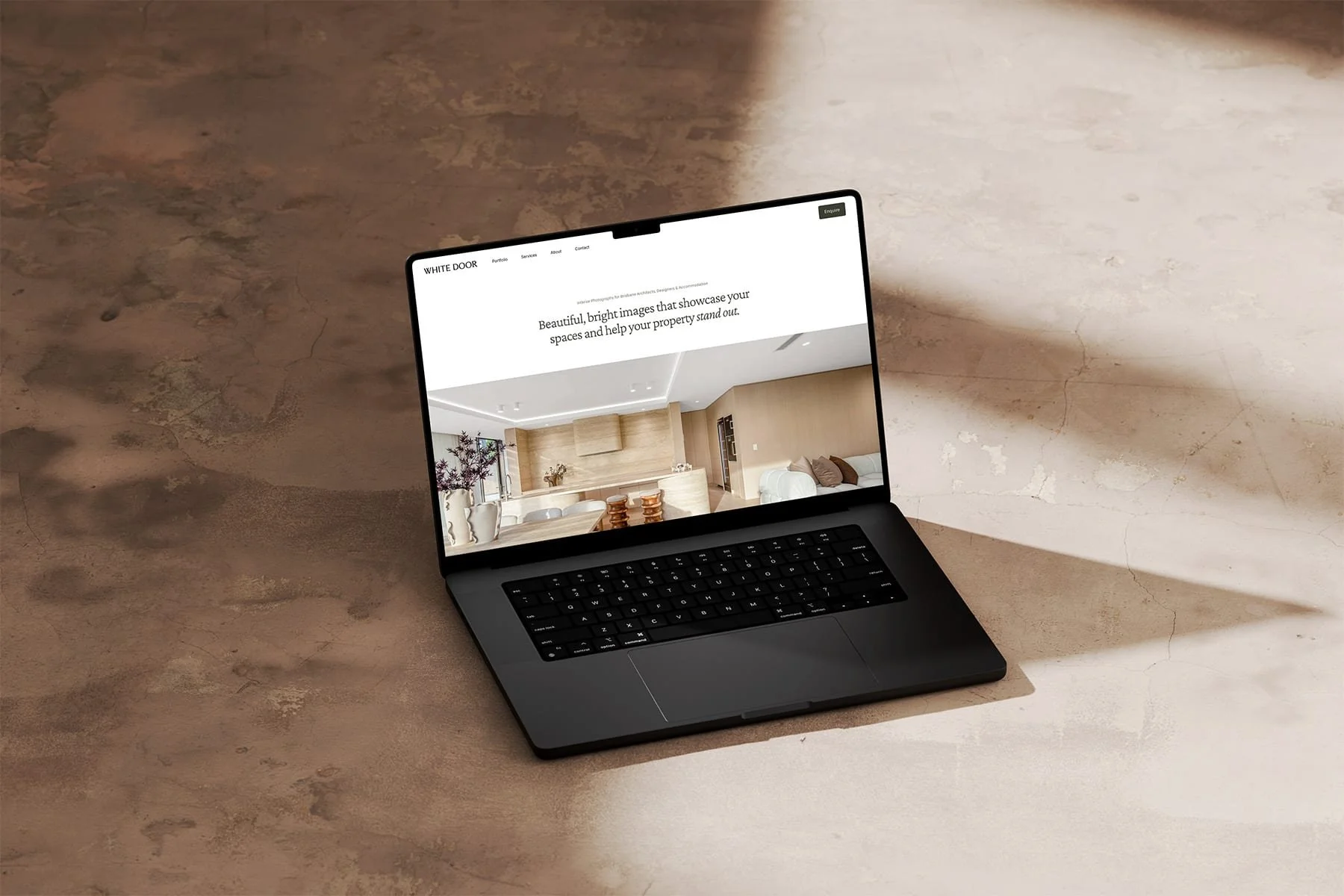Homepage website design for White Door Photography showing an open Macbook on a concrete surface with a modern minimalist layout showcasing interior photography