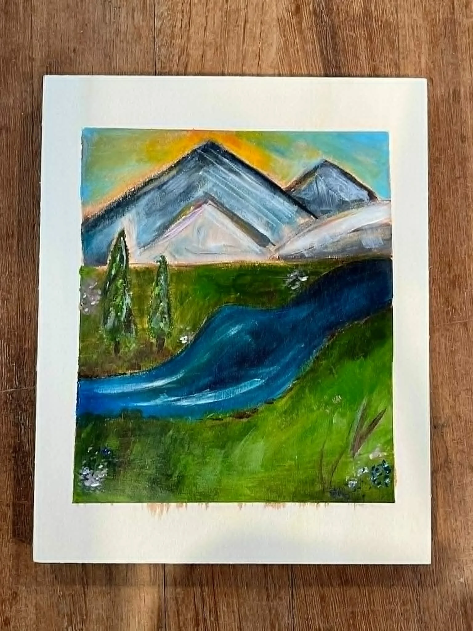 Watercolor painting of mountains with colorful sky and green landscape in foreground.