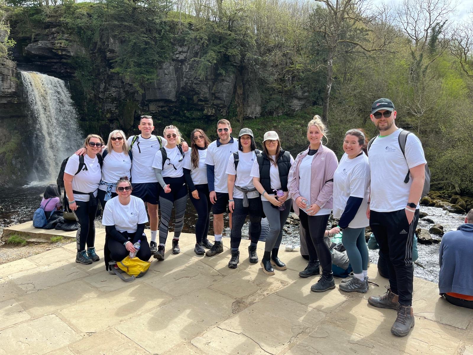 Group of people posing for a photo outdoors near a waterfall and river, with trees and rocks in the background.