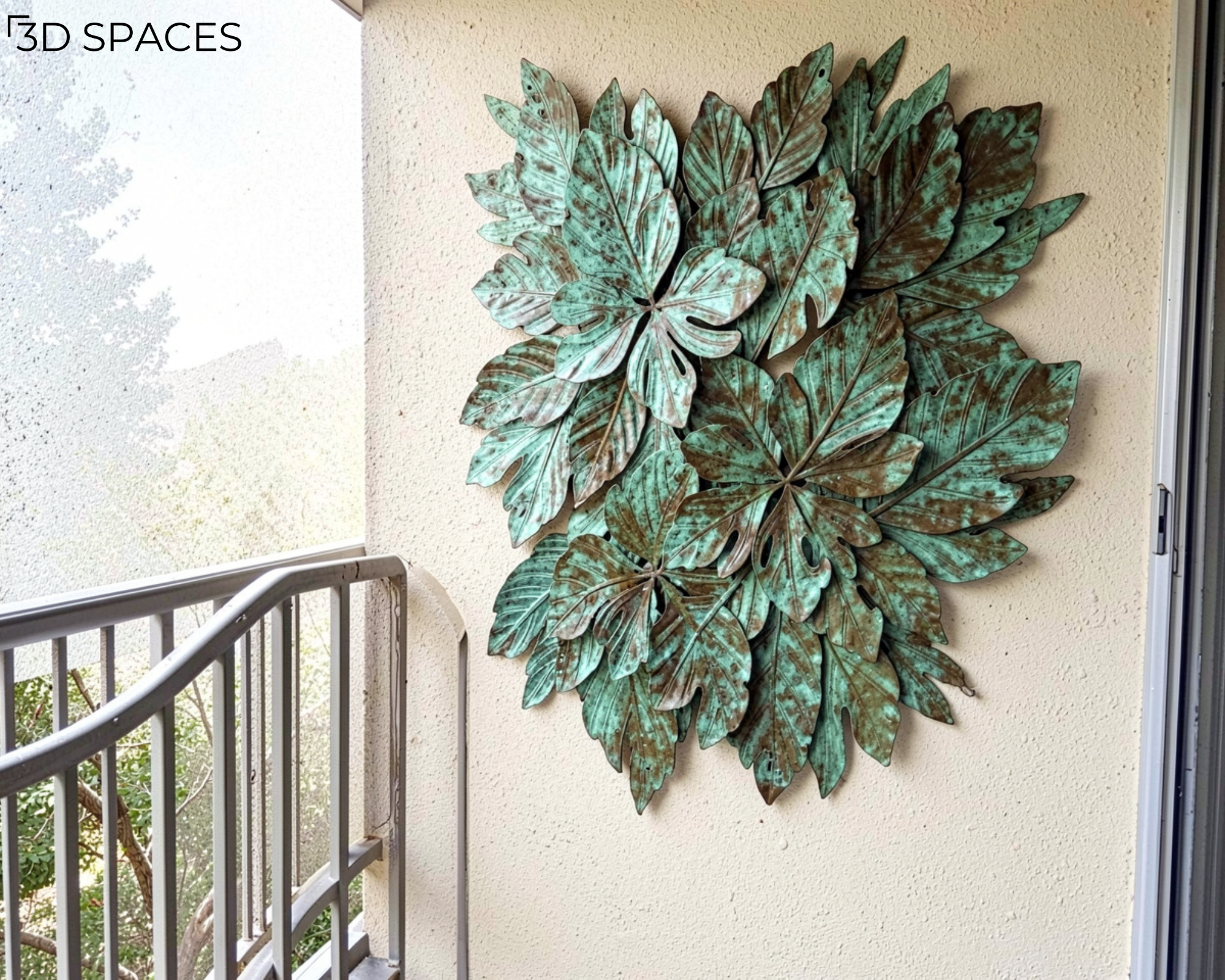 Large verdigris metal leaf wall art sculpture hanging on a stucco apartment balcony wall next to a railing.