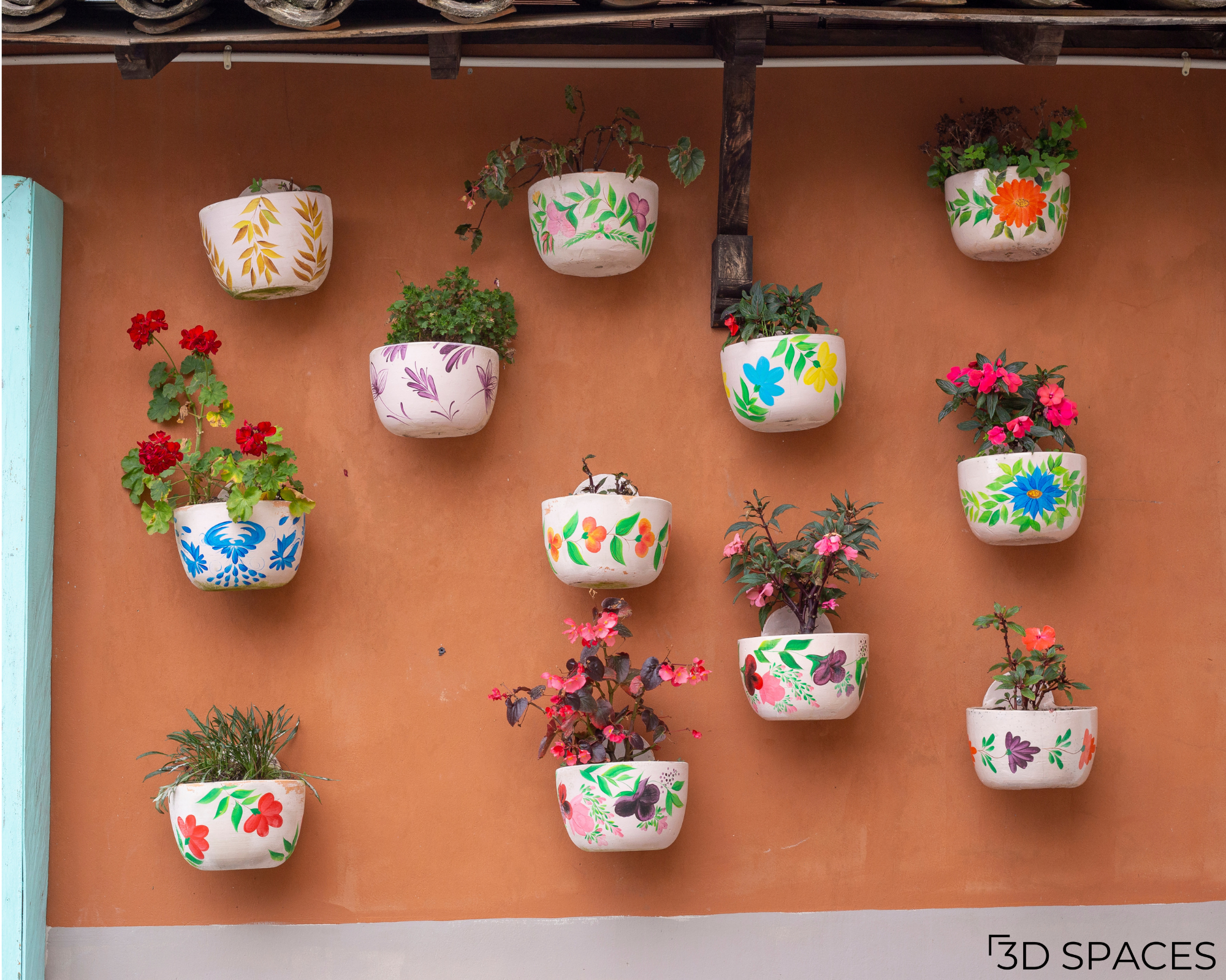 Hand-painted wall-mounted flower pots with vibrant floral artwork and colorful plants creating a decorative vertical garden on an outdoor wall.
