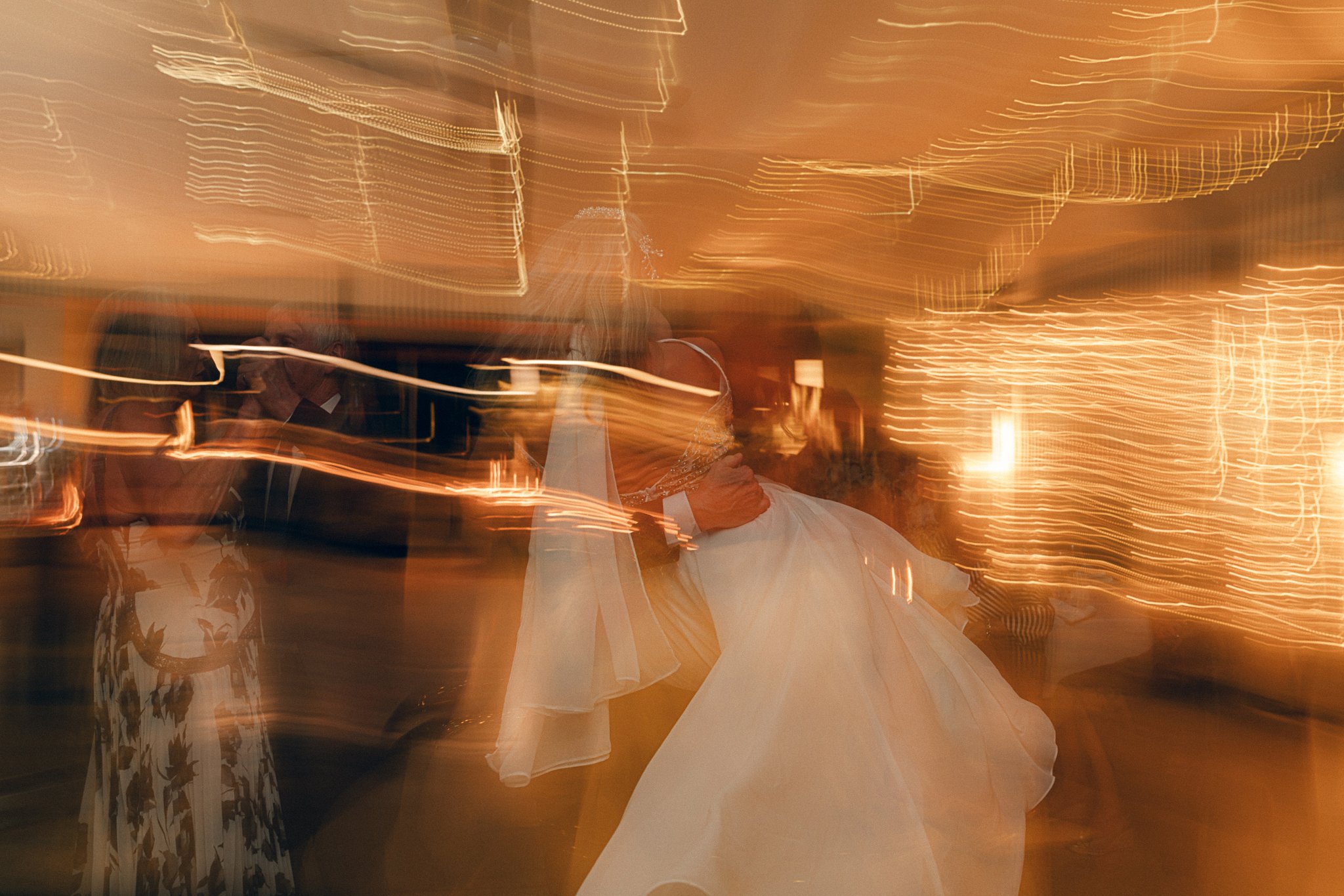 People dancing at a festive event with warm lighting and blurred motion effects.
