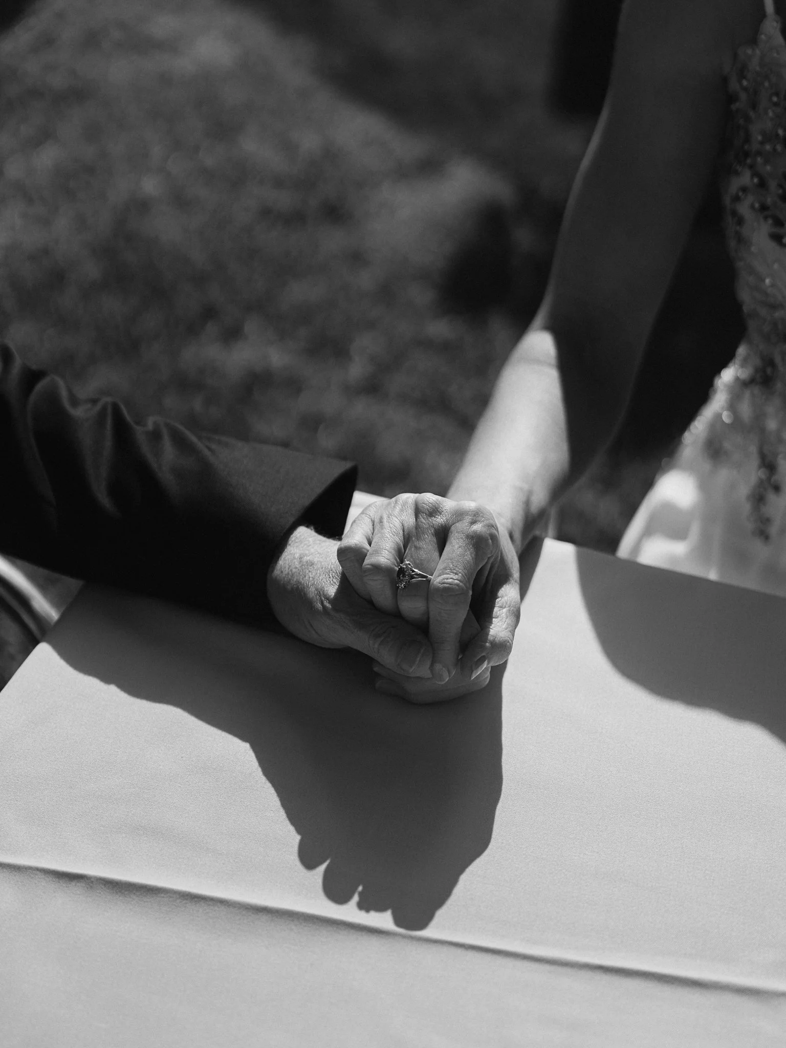 Close-up of an elderly couple holding hands, showing the woman's wedding ring, at a table during a wedding ceremony.