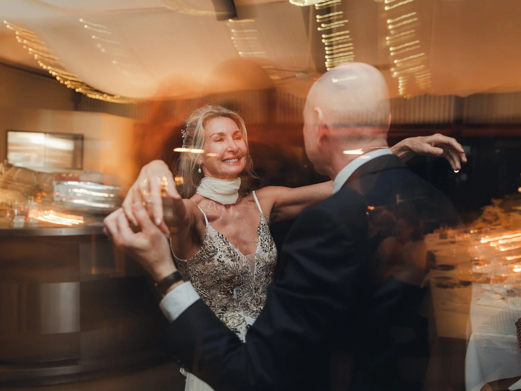 A woman in a fancy dress dancing with a man in a tuxedo at a wedding reception.