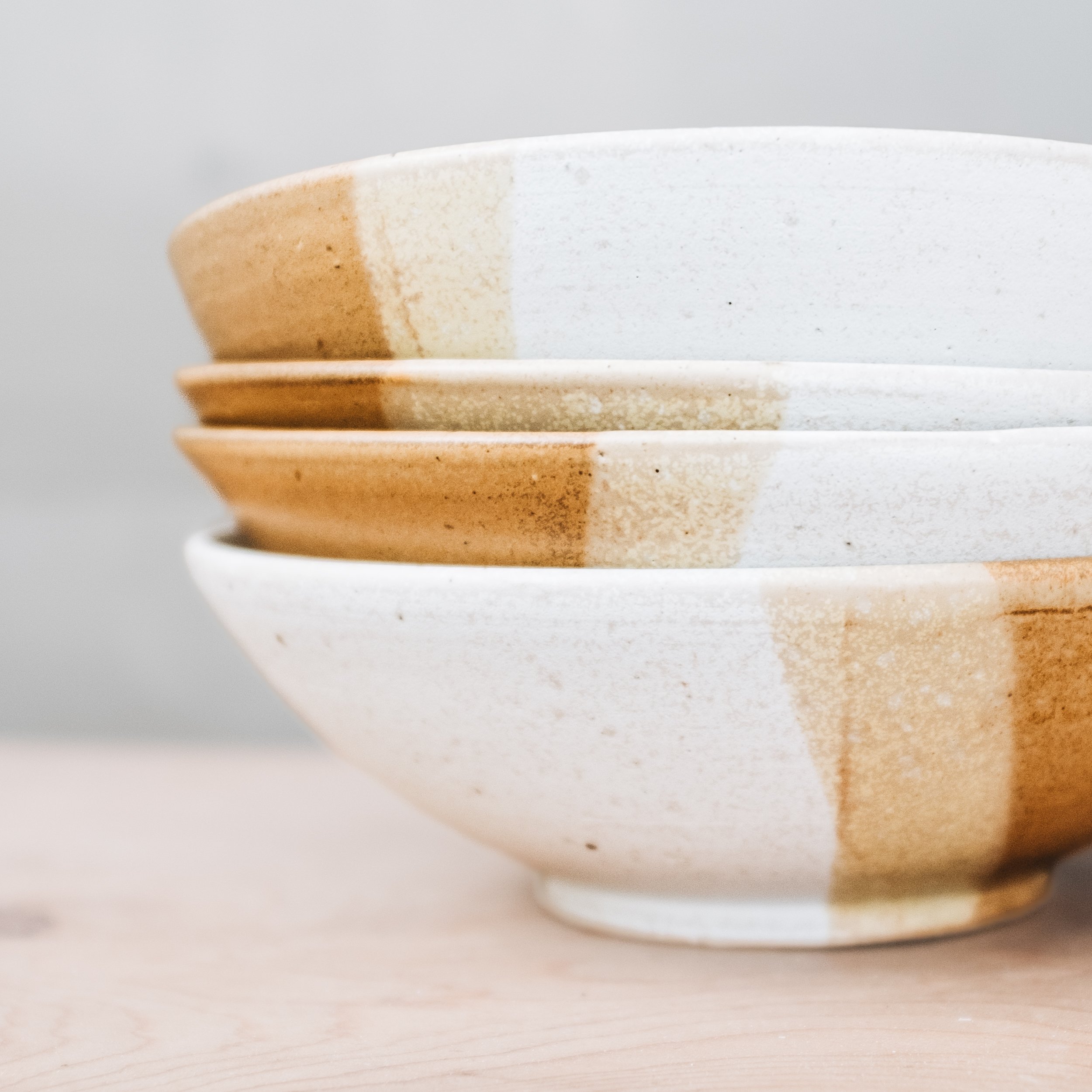 Stack of four ceramic bowls with a white and brown glazed finish, on a wooden surface.
