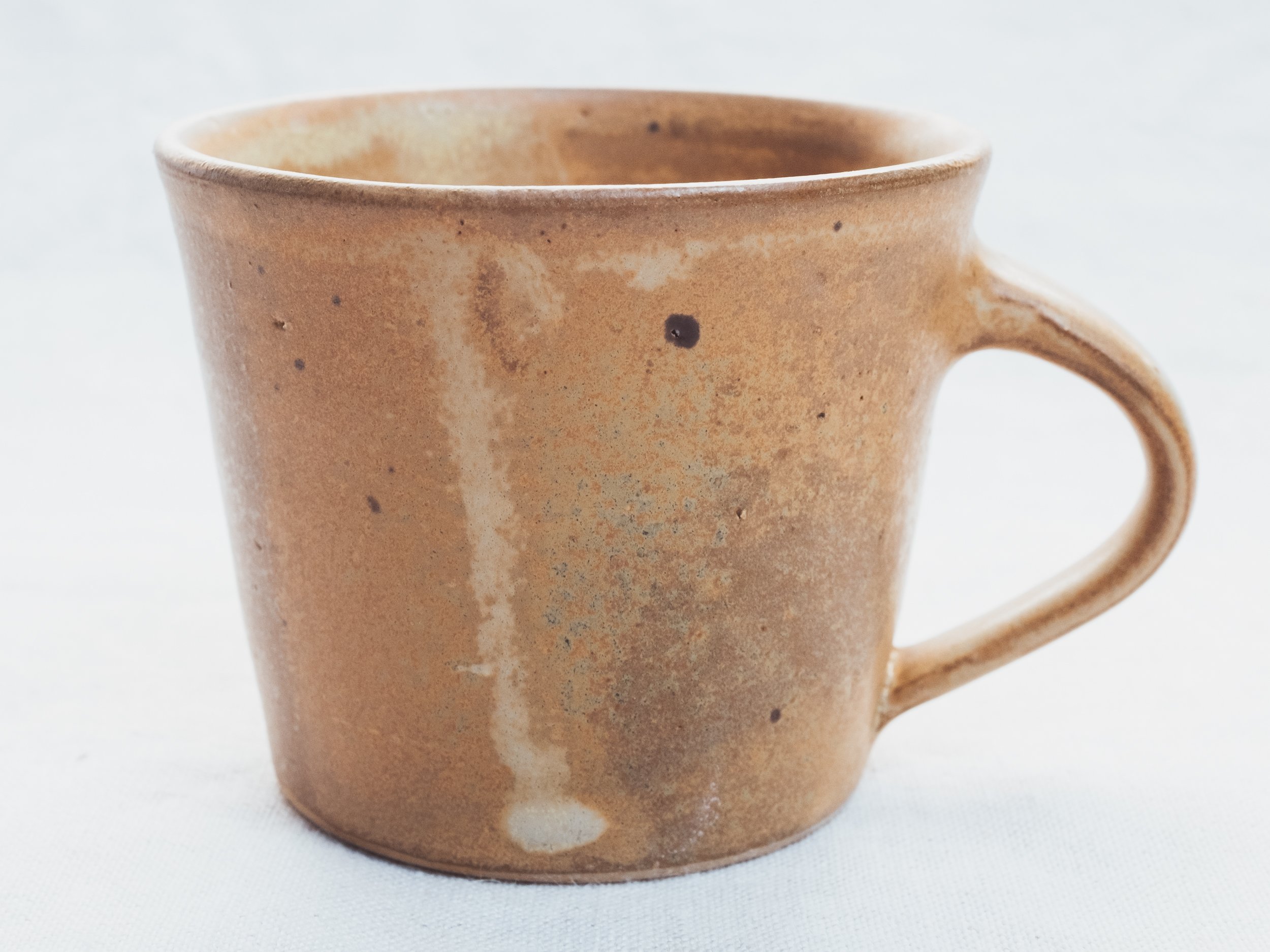 Ceramic coffee mug with a brown speckled glaze on a light background.