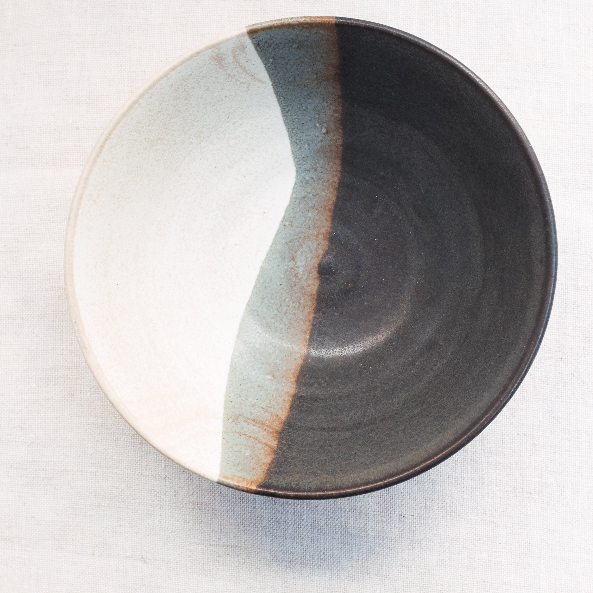 Ceramic bowl with split color design in black and beige on a pale fabric background.
