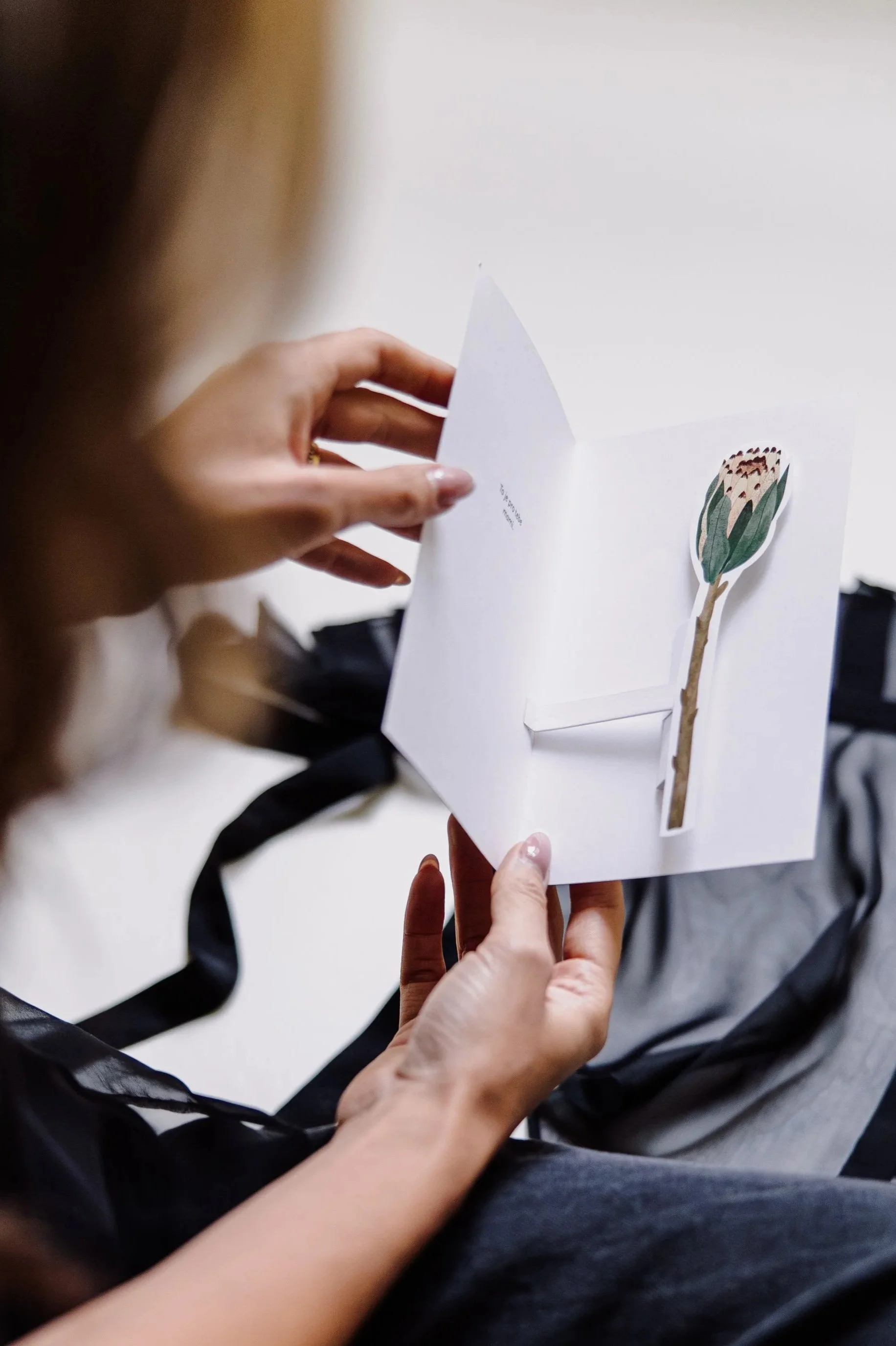 Person holding an open greeting card with a flower illustration inside.