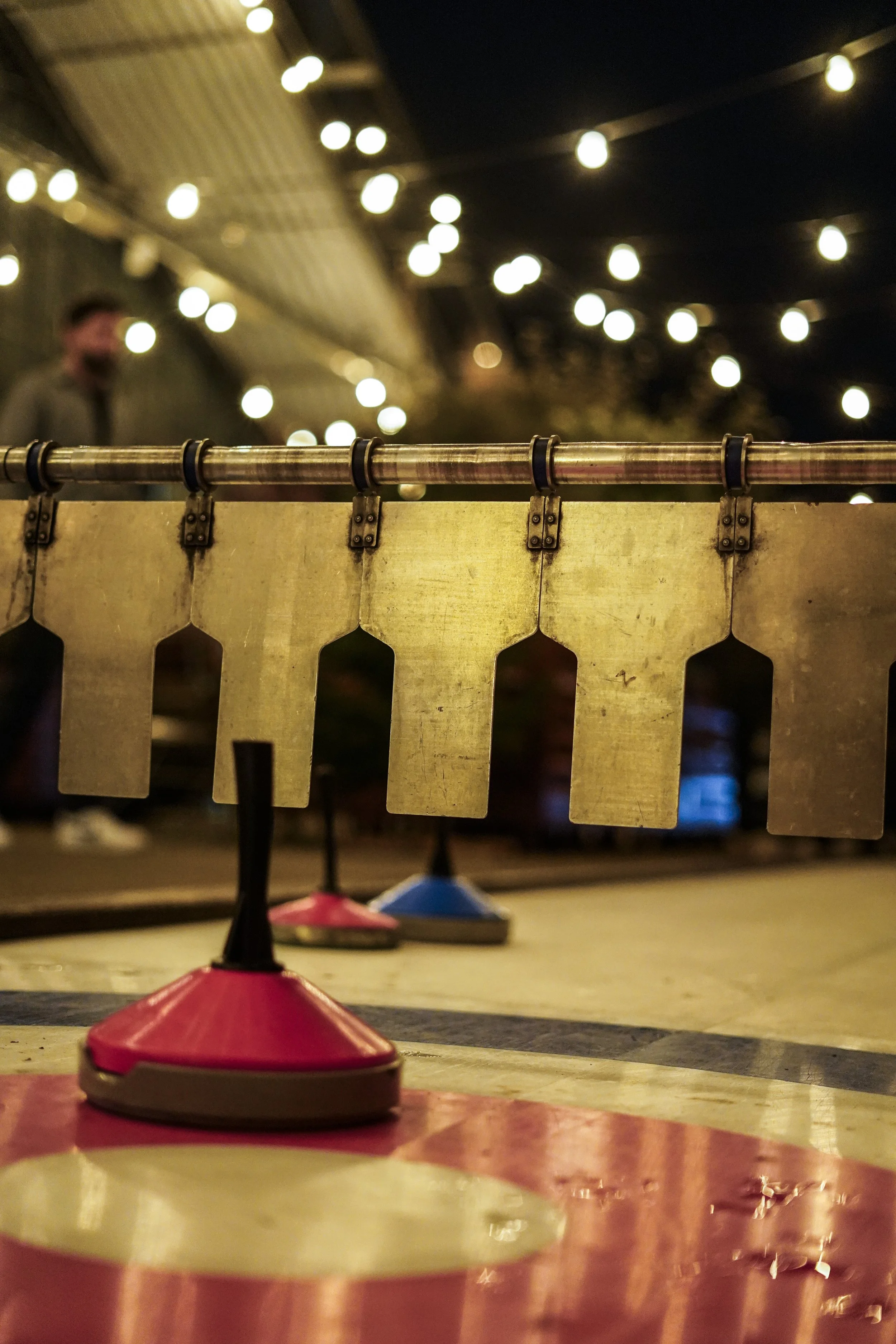 Bocciabahn mit roten und blauen Kegeln, Beleuchtung im Hintergrund, Polizist steht im Hintergrund in der Dämmerung.