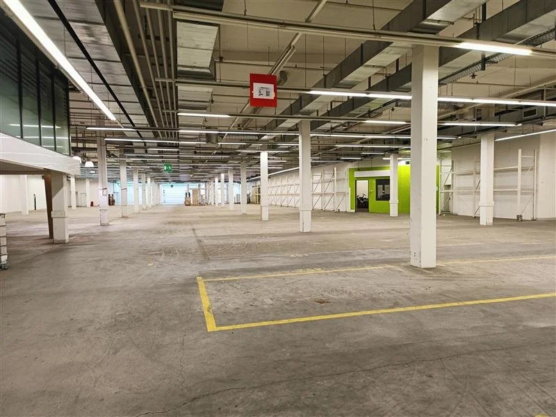 Leeres Parkhaus mit weißen Stützen, grüner Informationsstation und offenen Deckenansichten