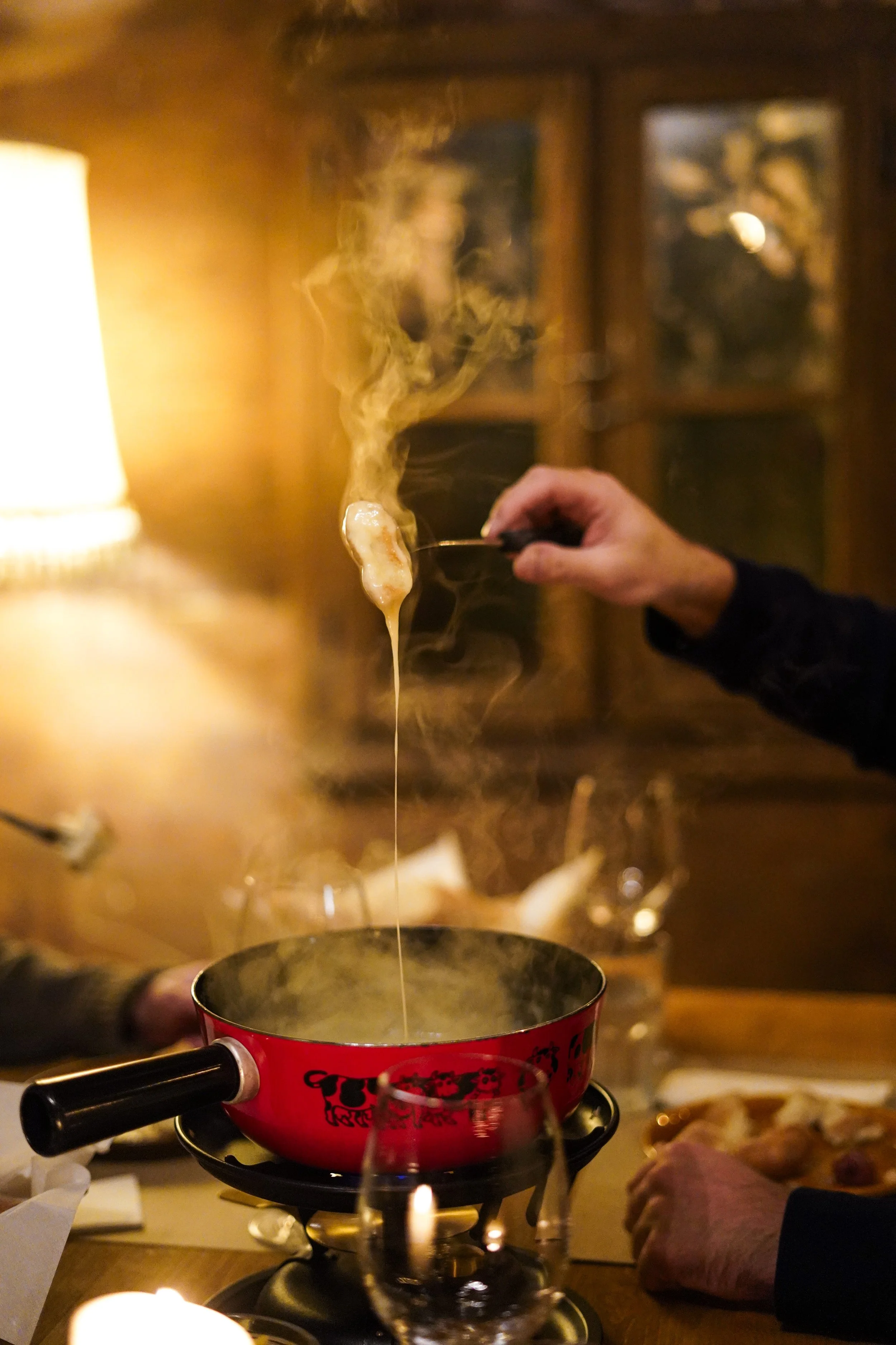 Person hebt einen geschmolzenen Käsefondue-Gabel mit Käse darüber, während er an einem romantischen Abend isst.