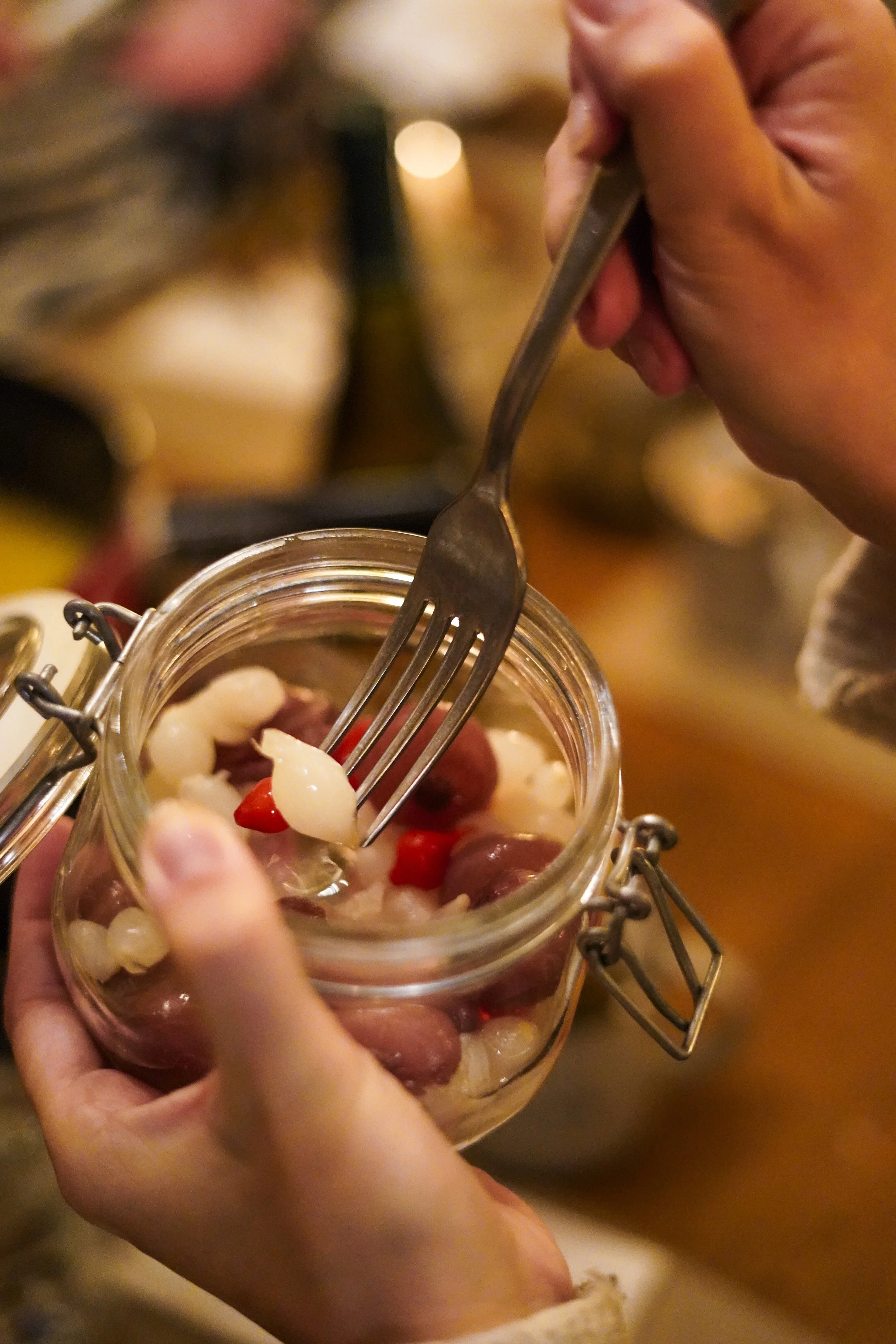 Person entnimmt eingelegtes Gemüse aus einem Glasgefäß mit einer Gabel.