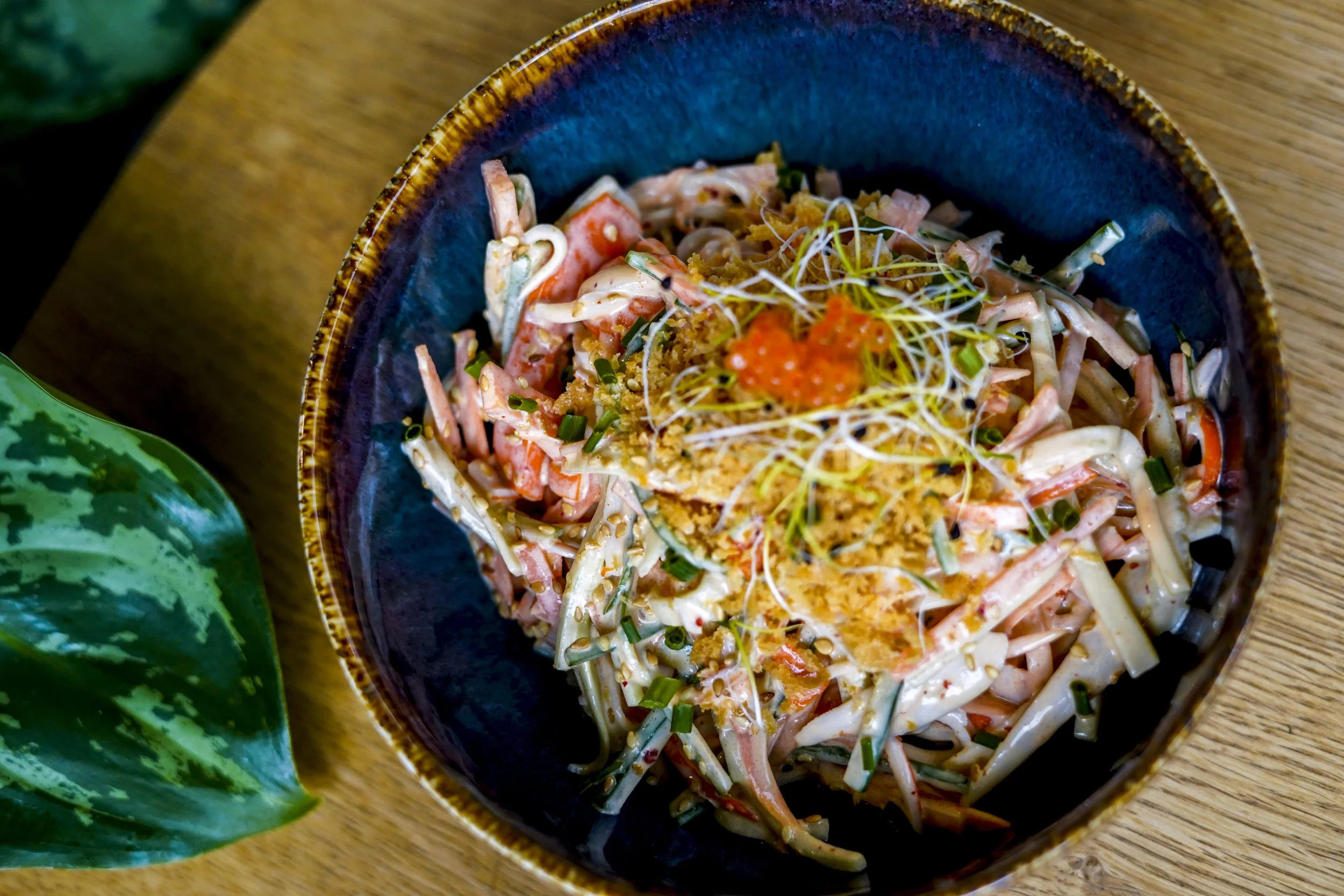 Schüssel mit Nudelsalat, garniert mit roten Kaviar, Sprossen und Gewürzen, auf einem Holztisch