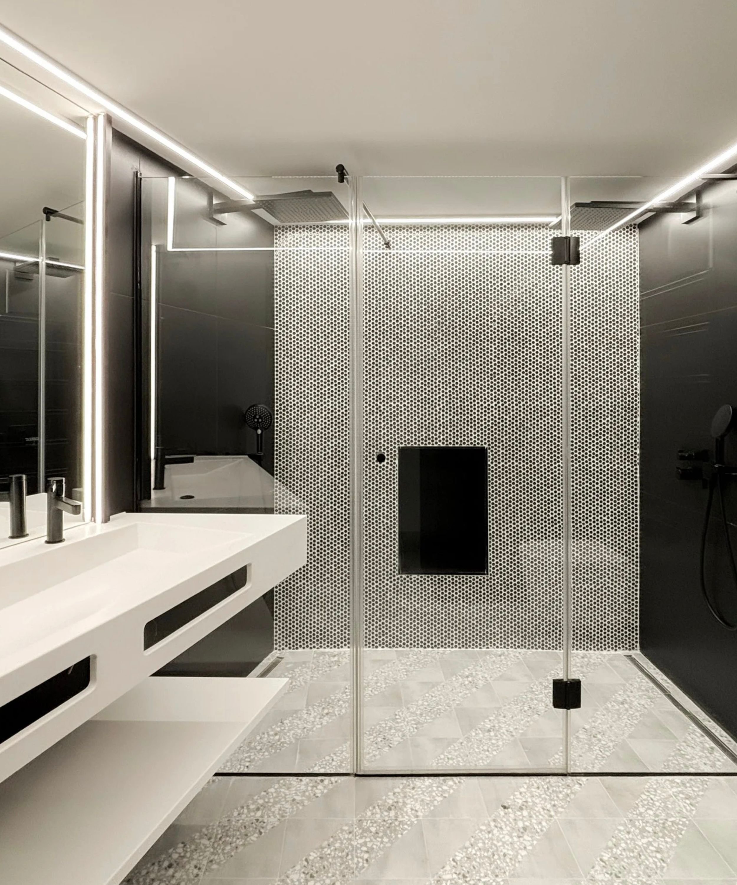 Modern bathroom with black and white color scheme, glass shower enclosure, white sink, and tiled floor.