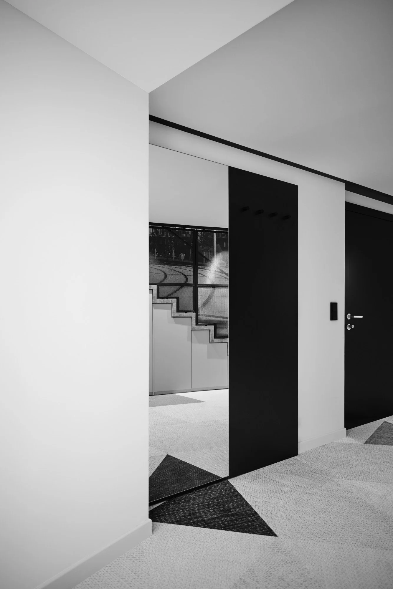 Interior hallway with modern black and white design, featuring a partial view of a staircase outside a glass window.