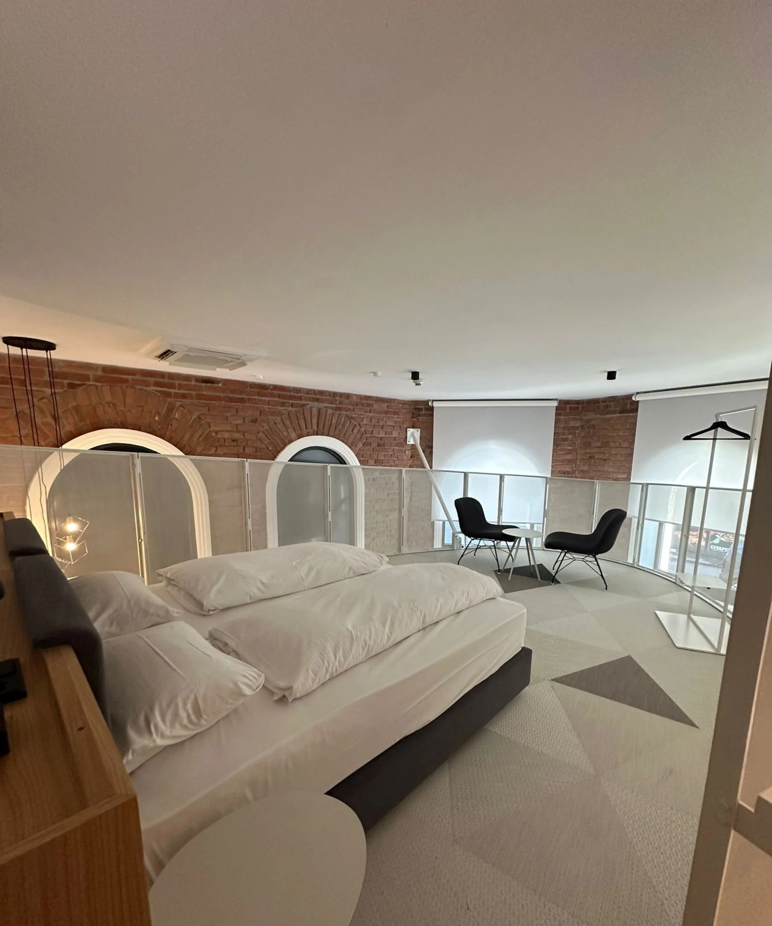 A bedroom with a bed, two black chairs, and a small white table near a glass window with an urban view.