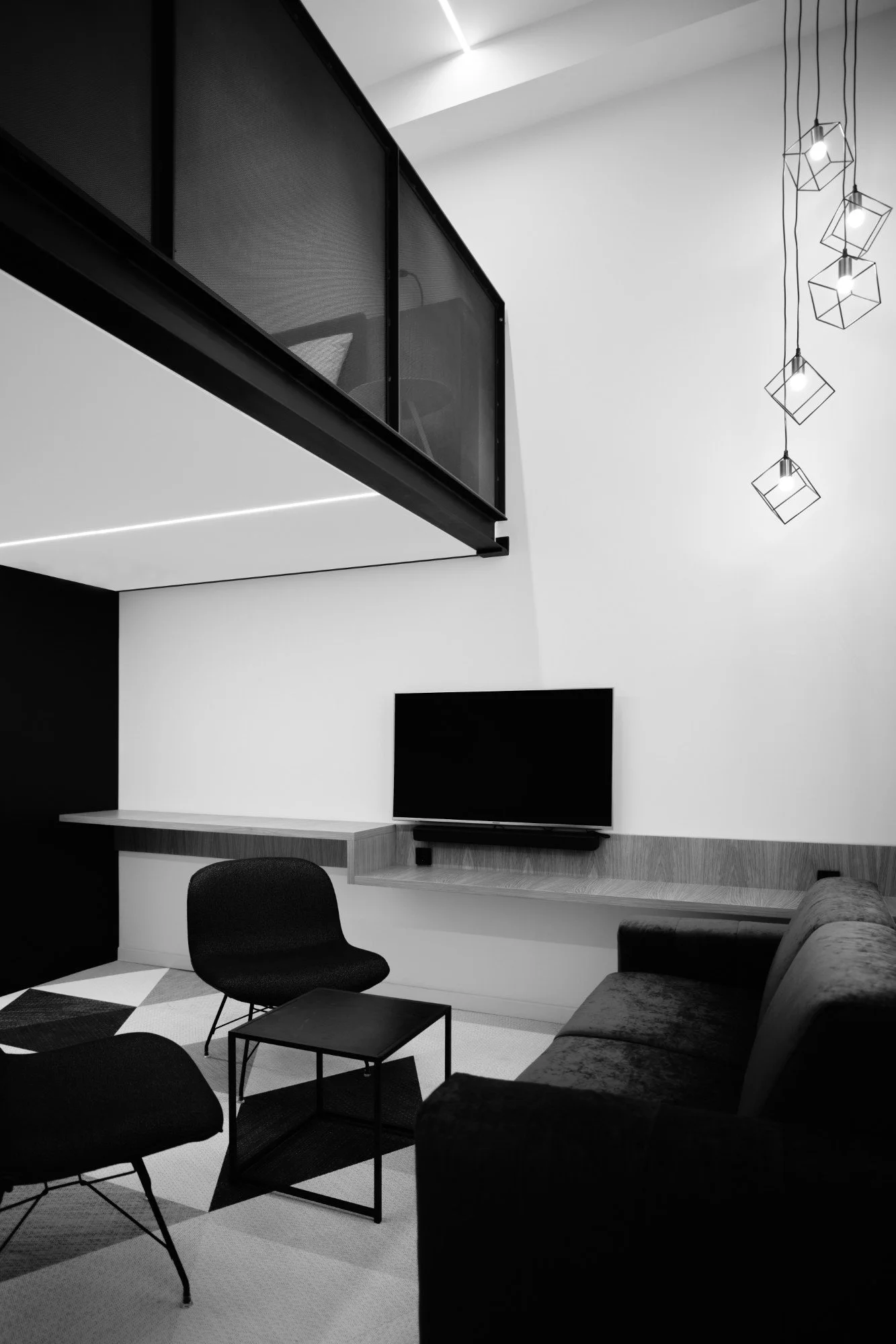Modern living room with black and white decor, a wall-mounted television, a black armchair, a sofa, and geometric ceiling lights.