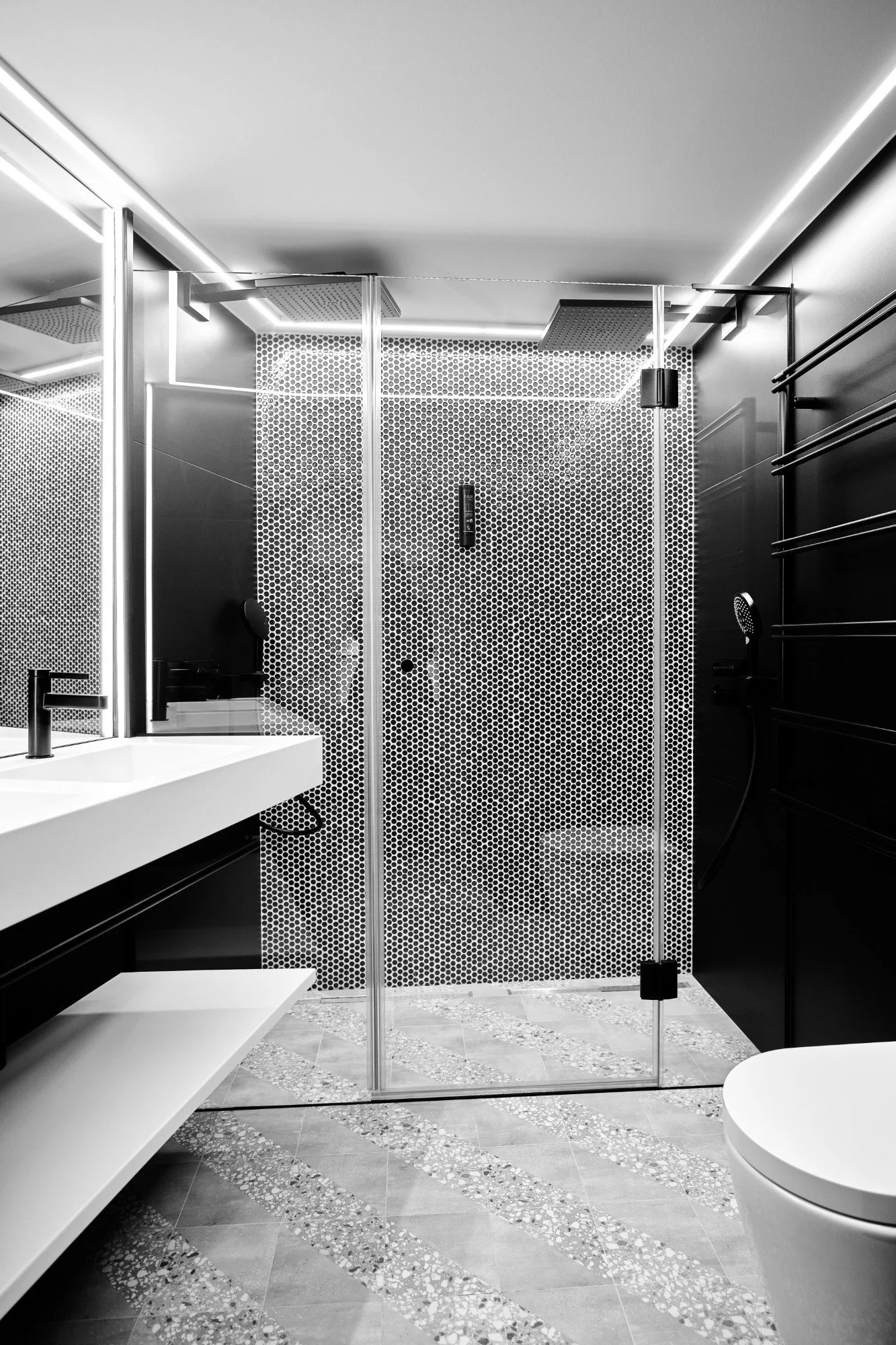 A modern bathroom with a glass-enclosed shower, black and white hexagonal tile wall, a white vanity with black fixtures, and a toilet, all in black and white color scheme.